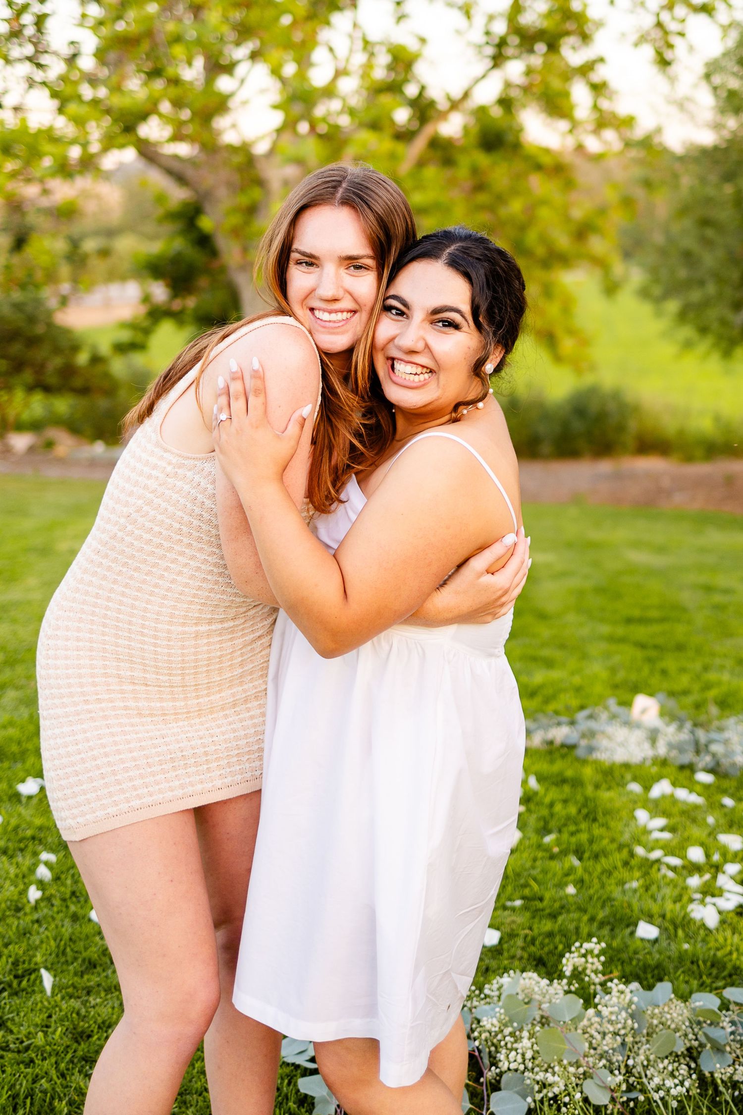 Friends sharing warm embrace on grassy lawn with wildflowers and garden backdrop.
