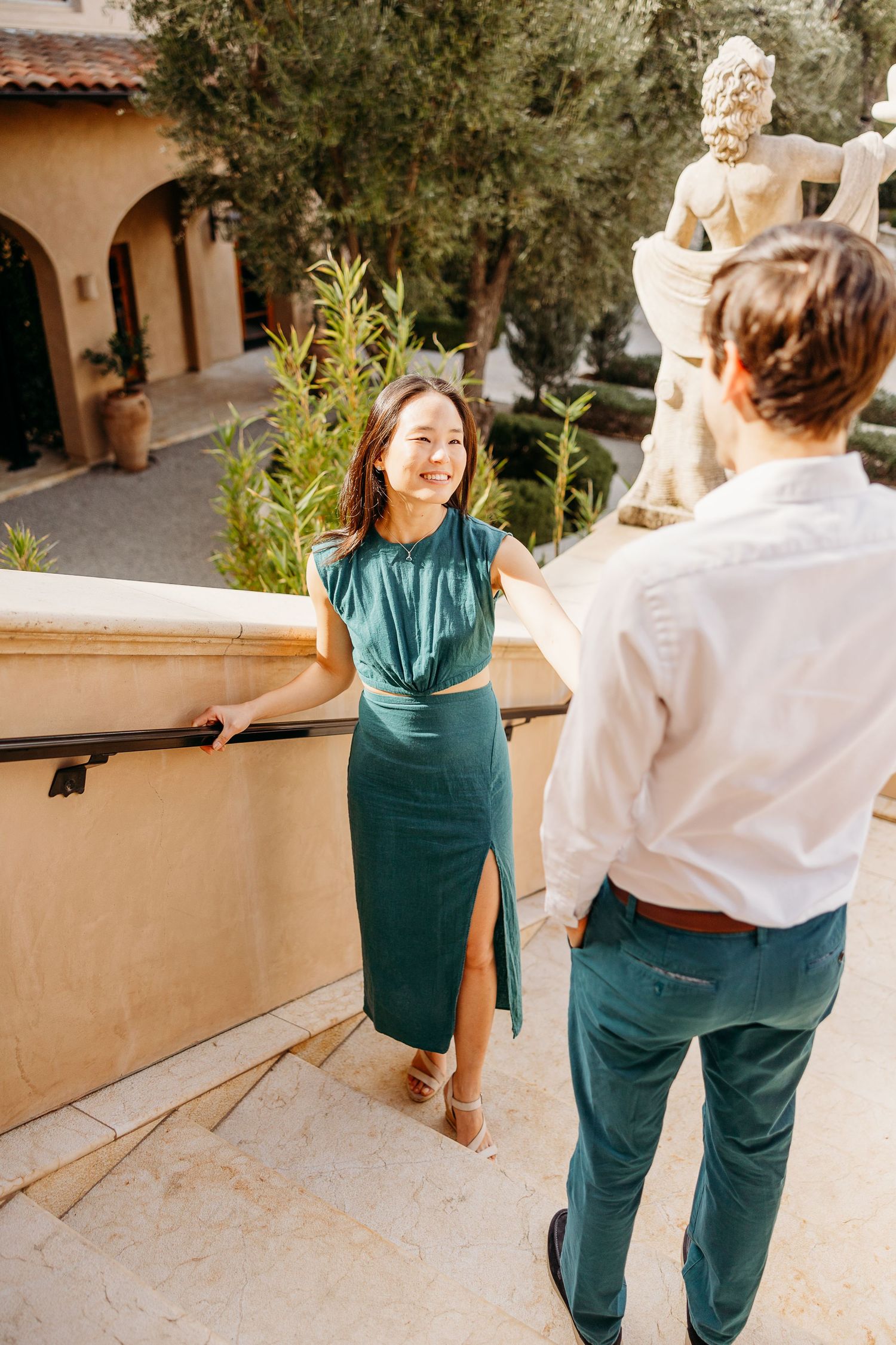 Couple having romantic moment on Mediterranean-style terrace with classical statue and greenery.