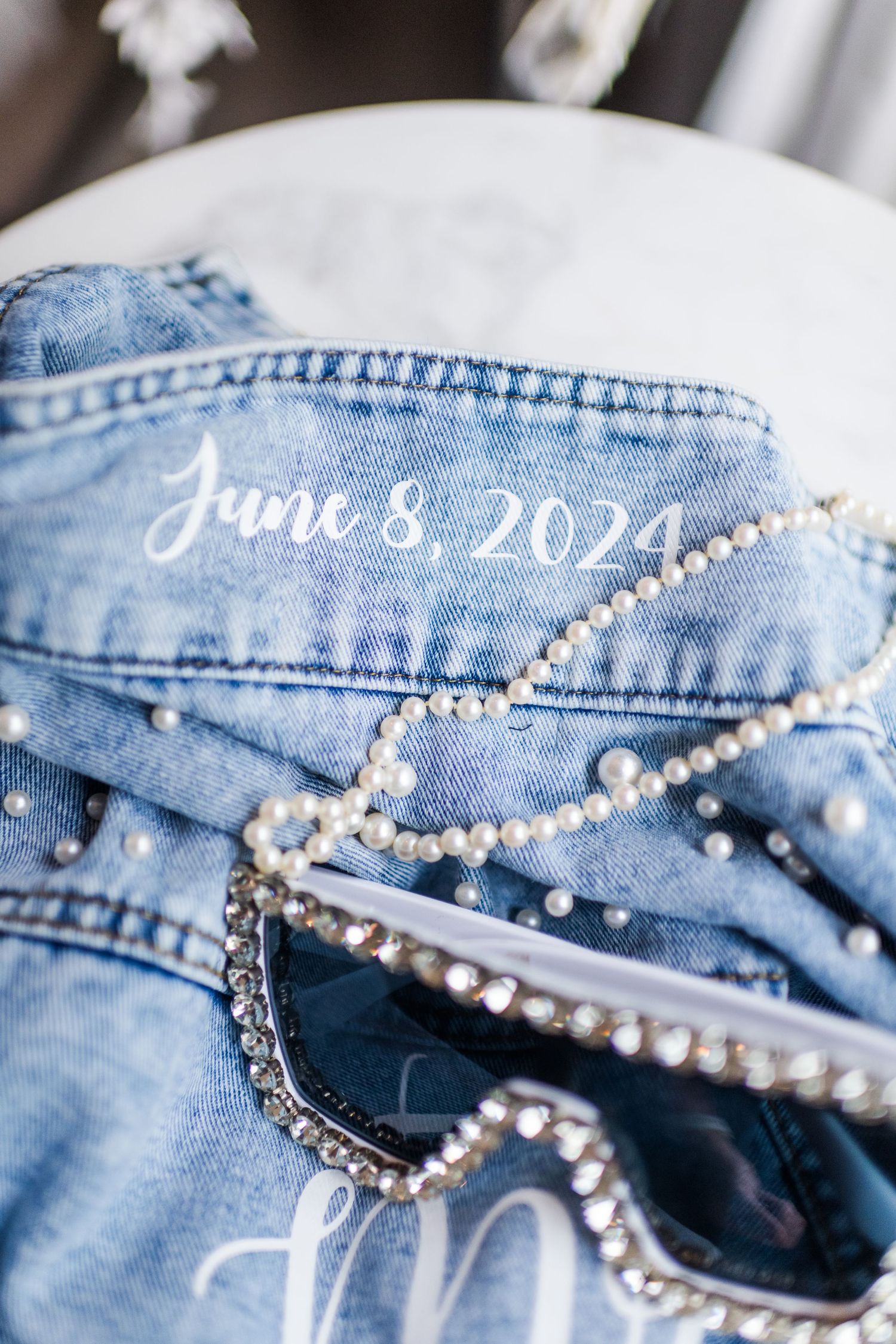Denim fabric with pearl decorations and 'June 8, 2024' text written in white.