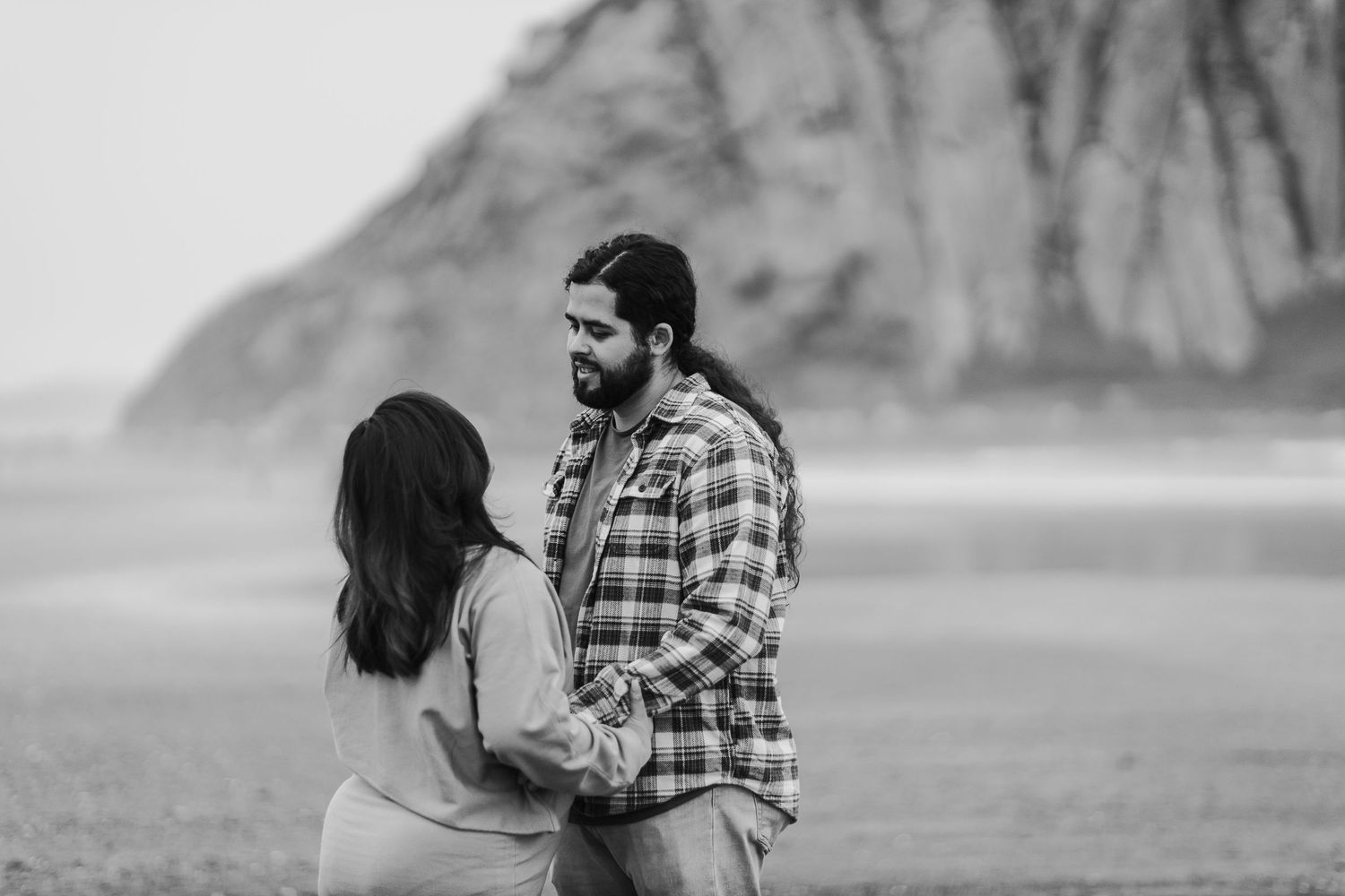 A couple shares a romantic moment together on a misty beach with dramatic cliffs in the background.