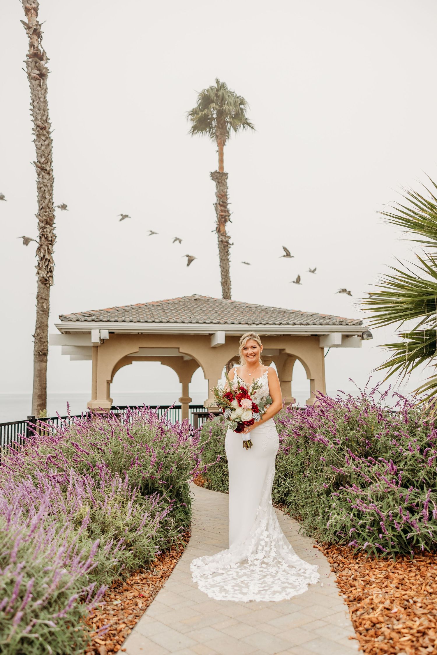 Coastal wedding scene with palm trees and flying birds framing elegant bridal portrait.