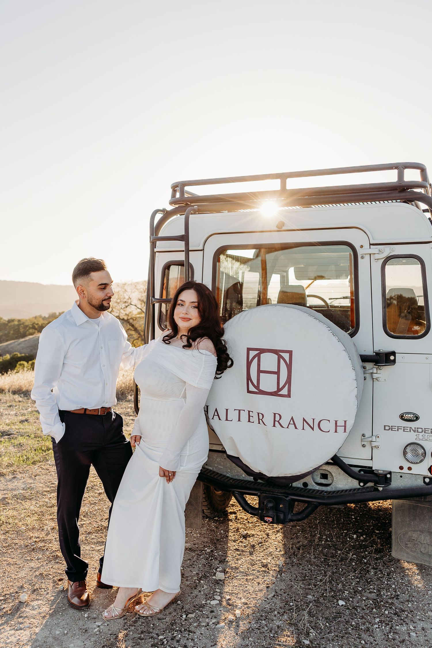 A couple shares romantic moments at sunset near a vintage Alter Ranch trailer in a desert setting.