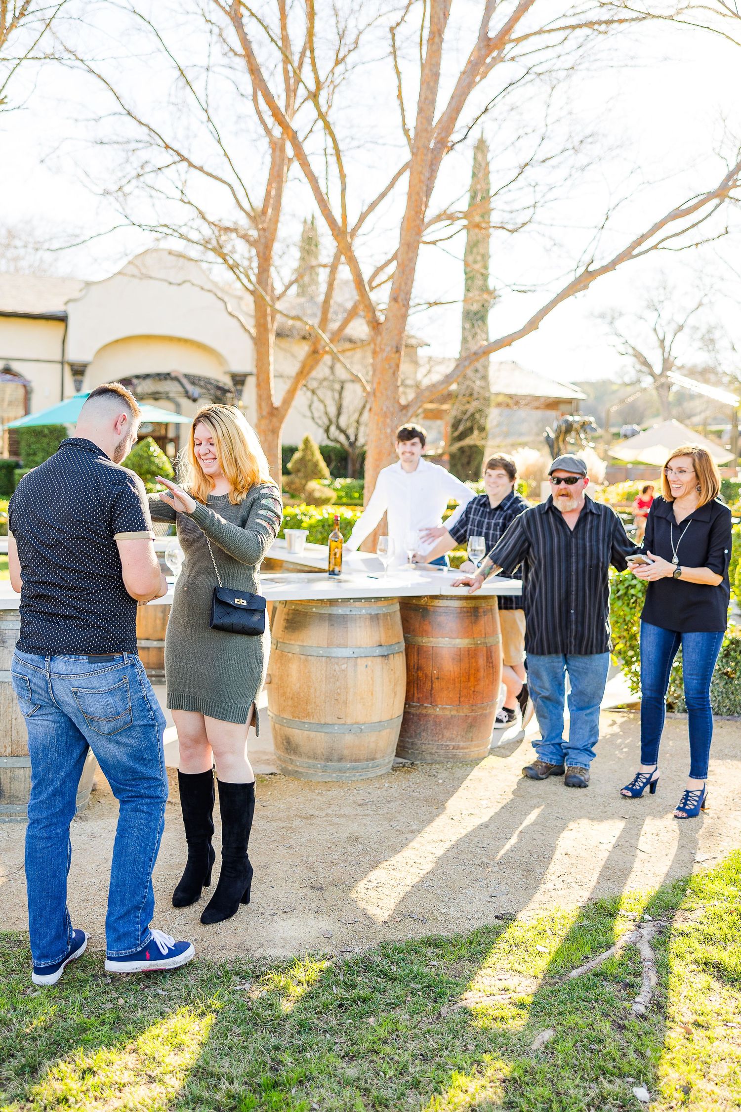 A sunny afternoon celebration at a winery with wooden barrels and groups of people enjoying the moment.