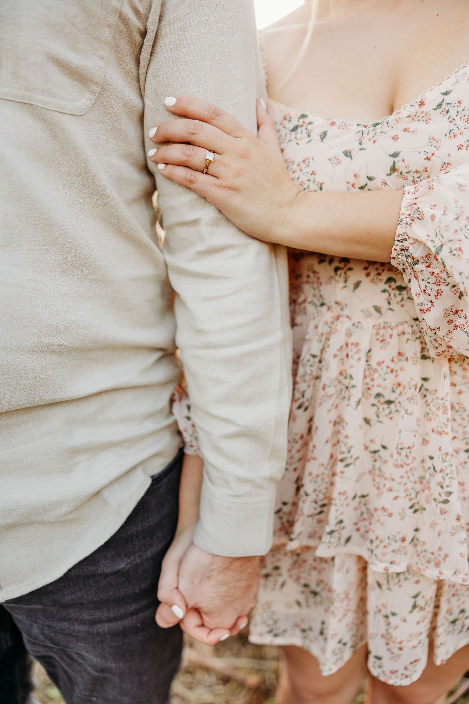 Close-up detail of hands holding and engagement ring in romantic outdoor setting.