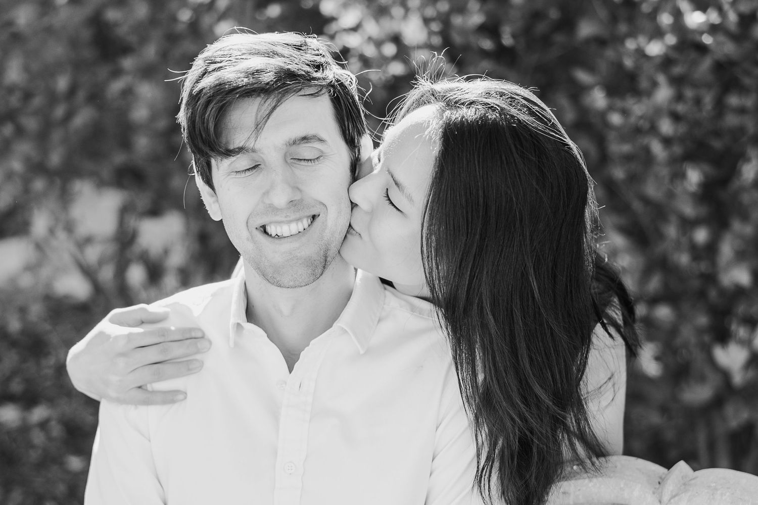 Black and white portrait of a couple sharing a joyful moment outdoors.