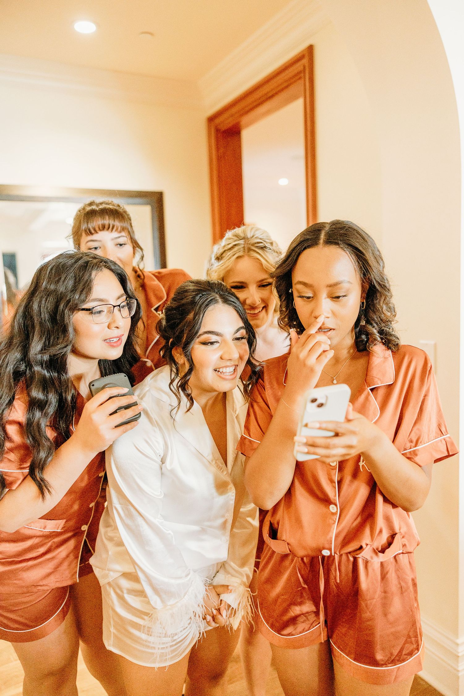 Group wearing silk robes looking at phone during wedding preparation.