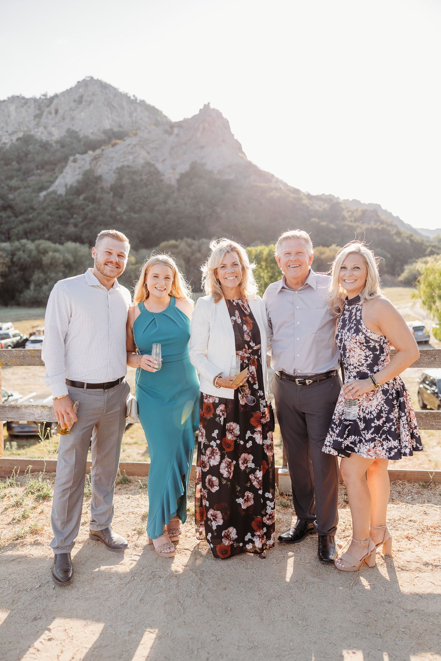 A group poses together at sunset in front of mountains, wearing elegant dresses and button-down shirts.