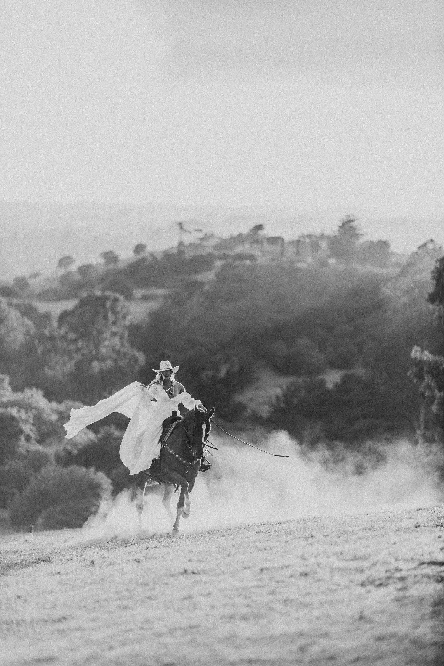 Dramatic black and white capture of a rider galloping through dusty mountain terrain.