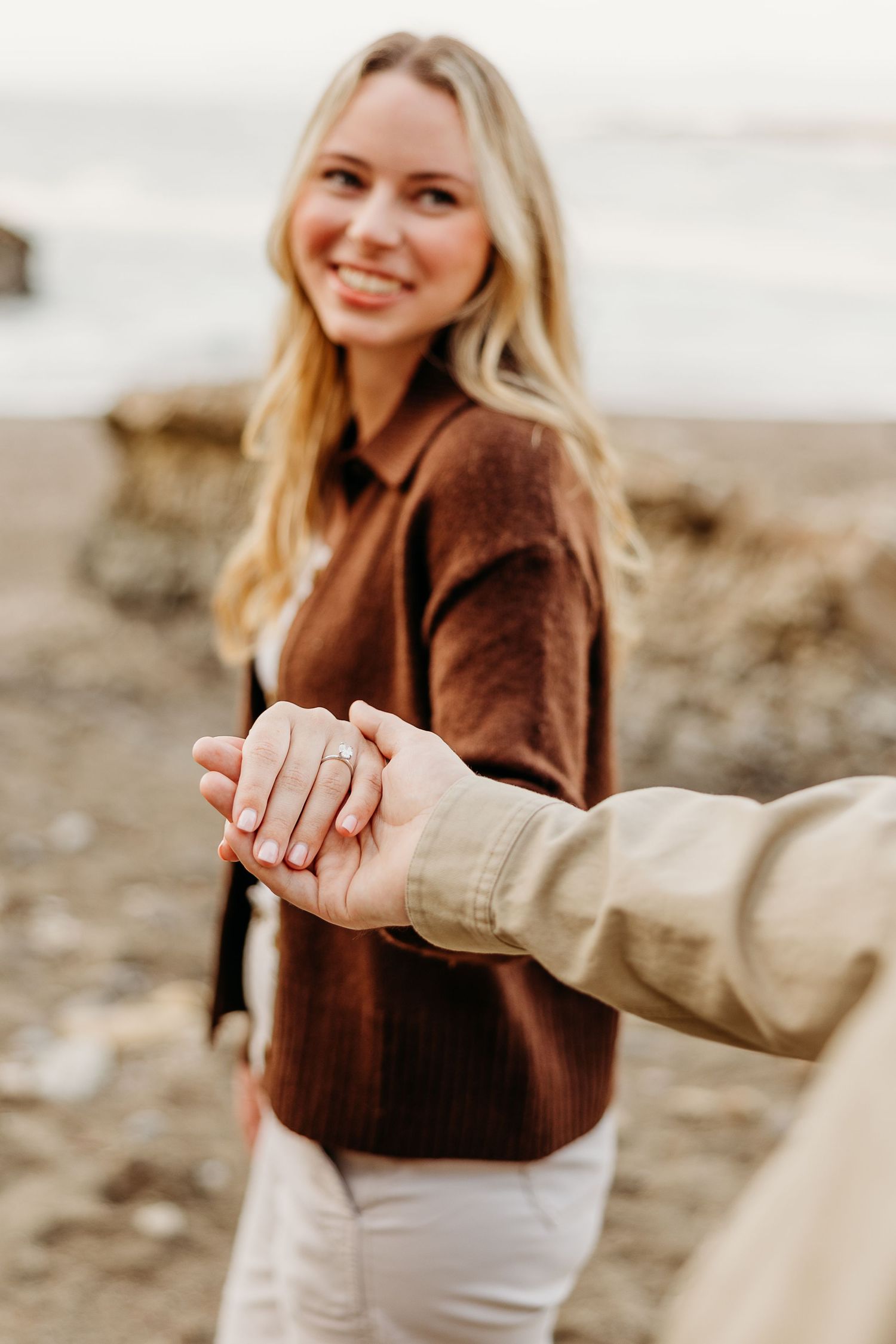 Close-up shot of hands showing off a new engagement ring on a beach.