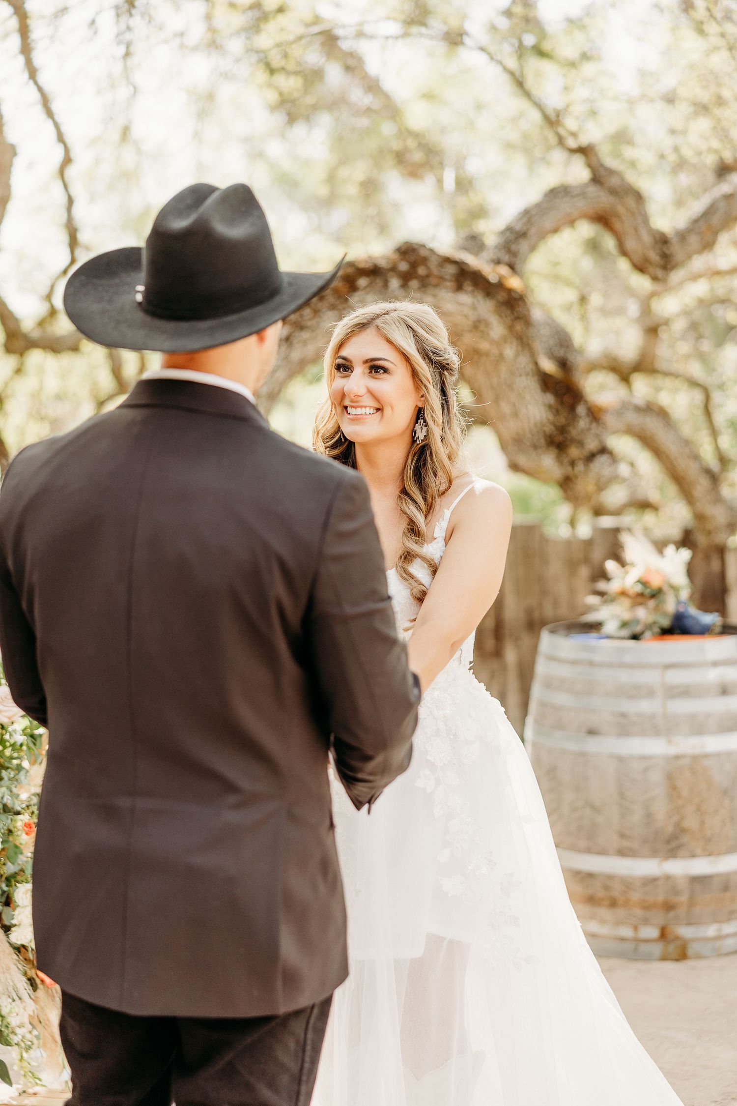 A couple shares a joyful moment during their rustic outdoor wedding near wine barrels.