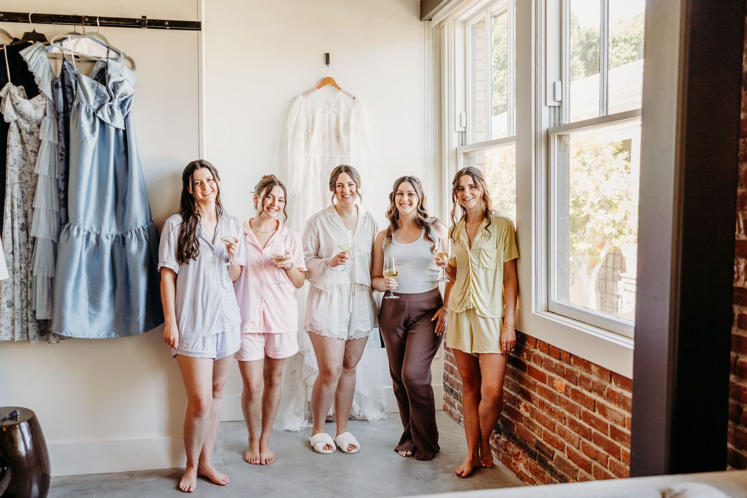Five people in light colored casual outfits stand together in a bright room with clothing racks behind them.
