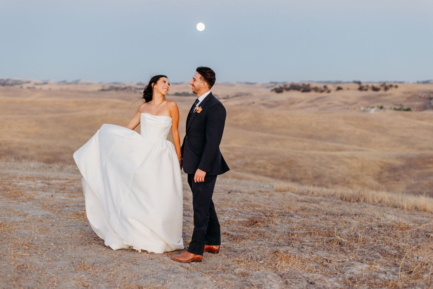 Newlyweds sharing intimate moments against a scenic desert landscape at sunset.