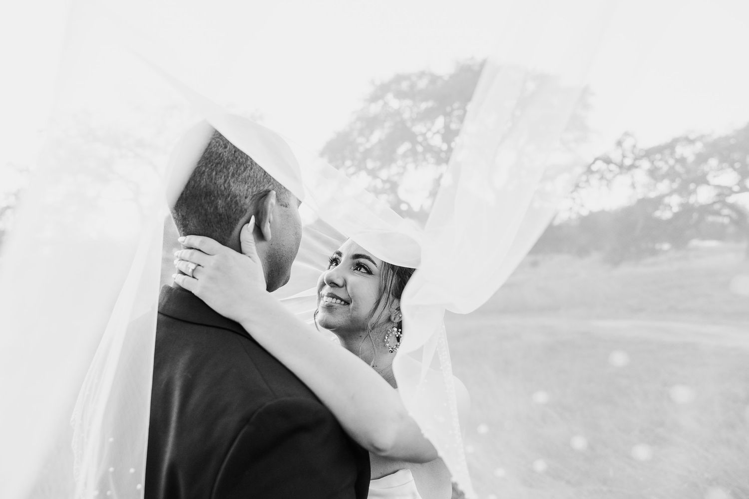 Romantic black and white portrait of a couple embracing outdoors with a bright background.