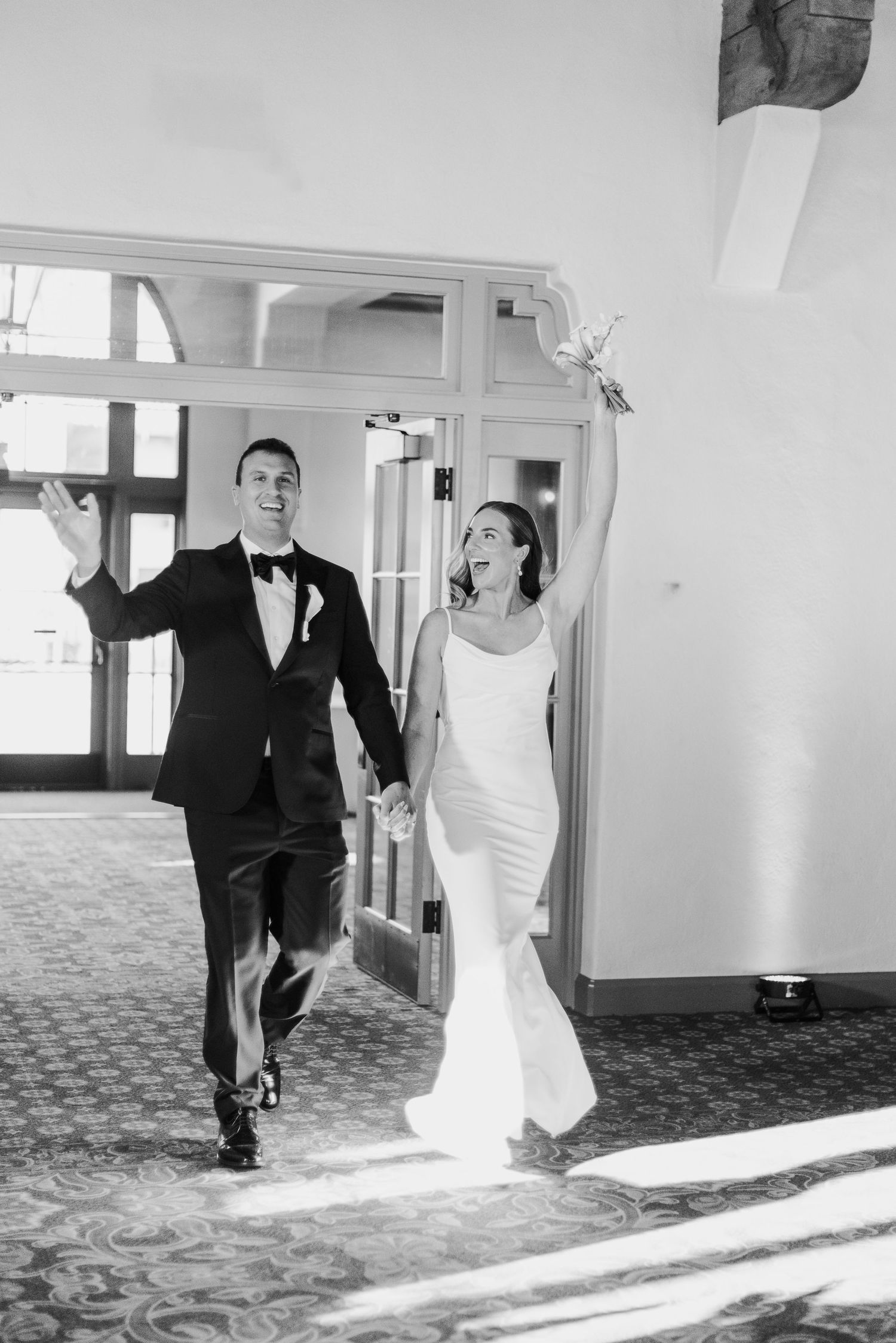 Black and white sequence shows a couple playfully running through a hallway at their wedding.