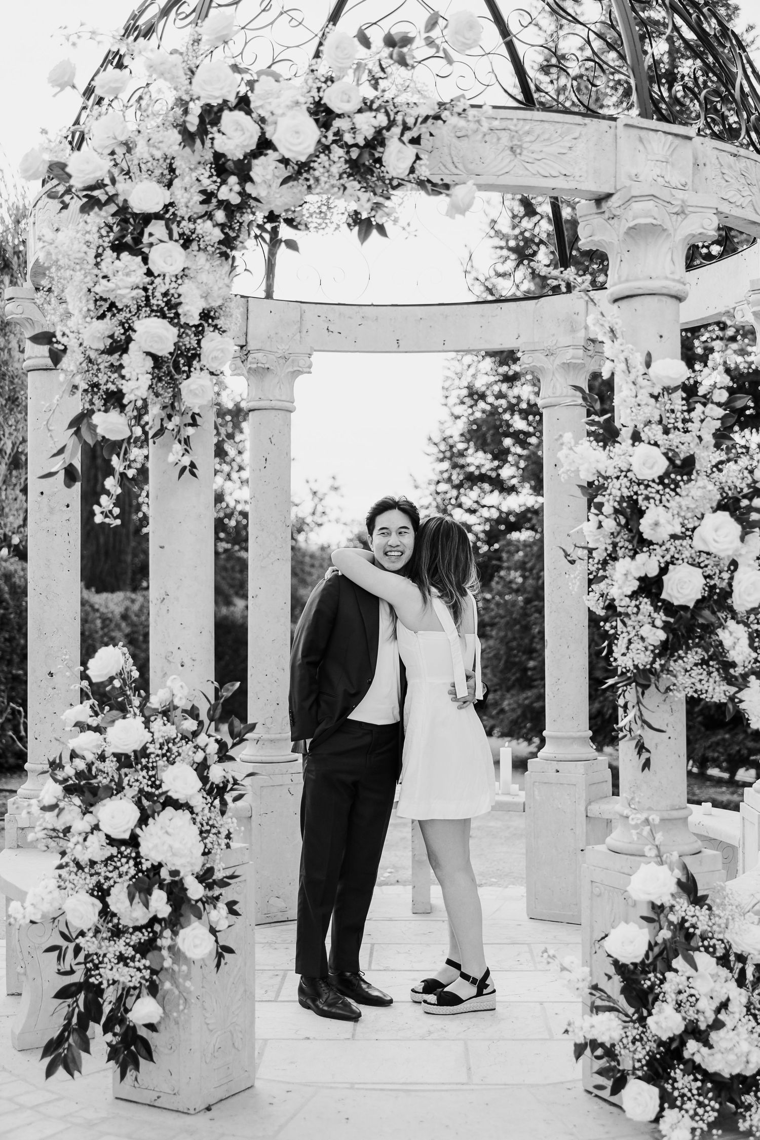 Black and white photo of a couple in an elegant white gazebo decorated with flowers.