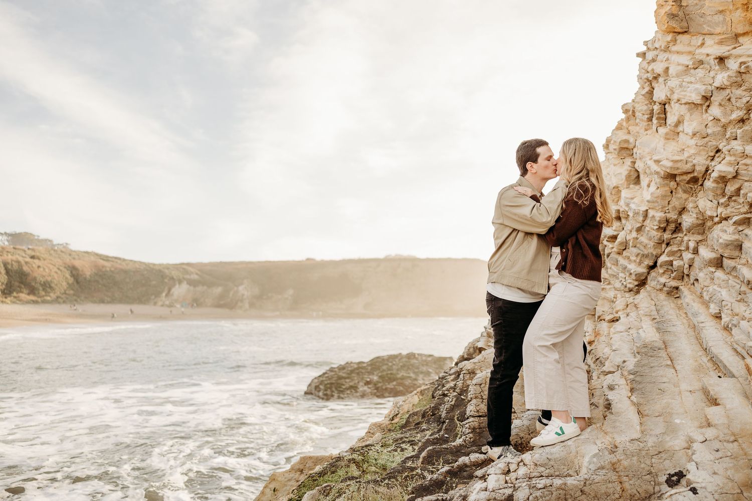 A couple shares an intimate moment on rugged ocean cliffs during a golden hour photoshoot.