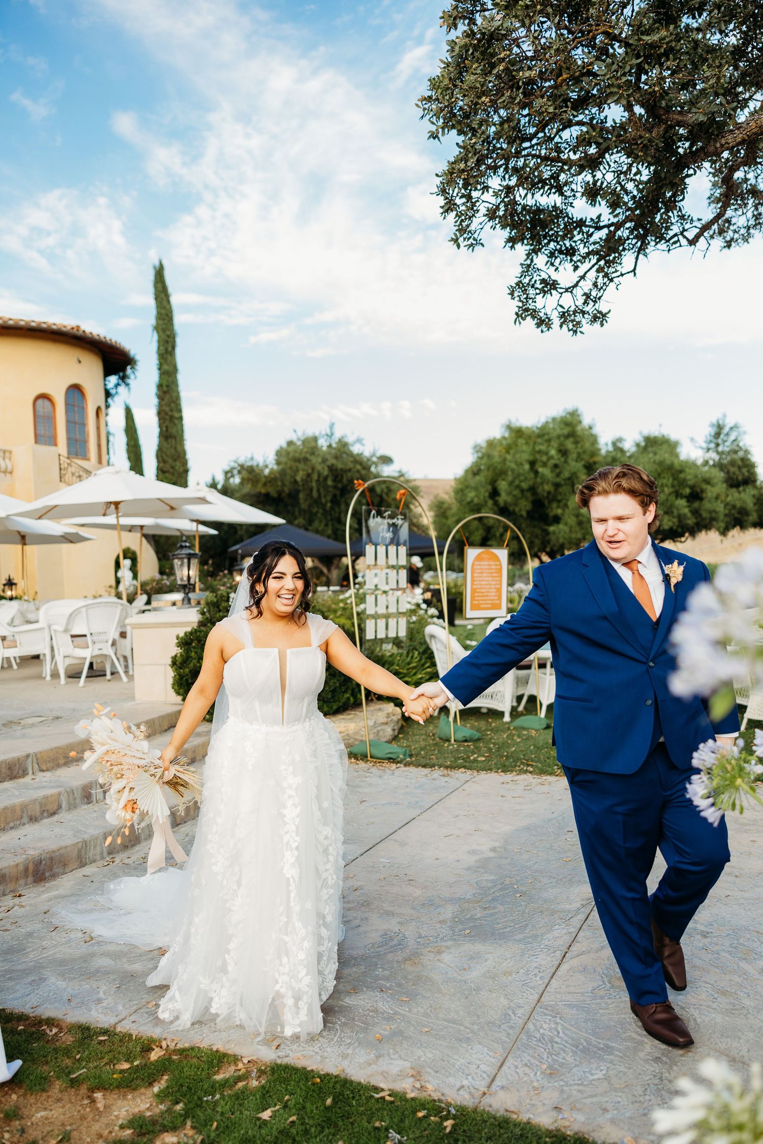 Newlyweds celebrate joyfully on stone steps with a Mediterranean villa and garden setting in the background.