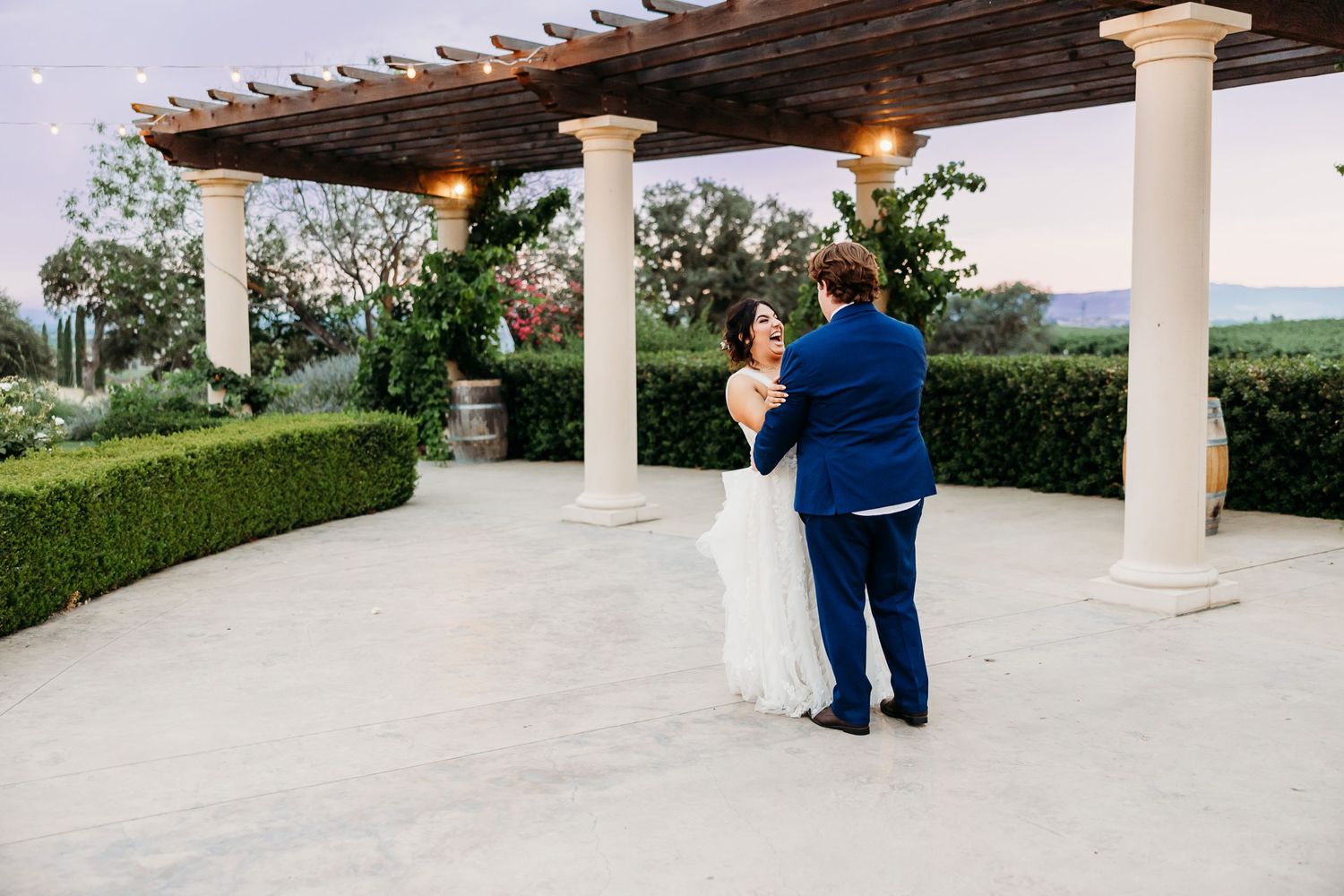 A couple shares a romantic moment under an elegant pergola overlooking scenic vineyard views.