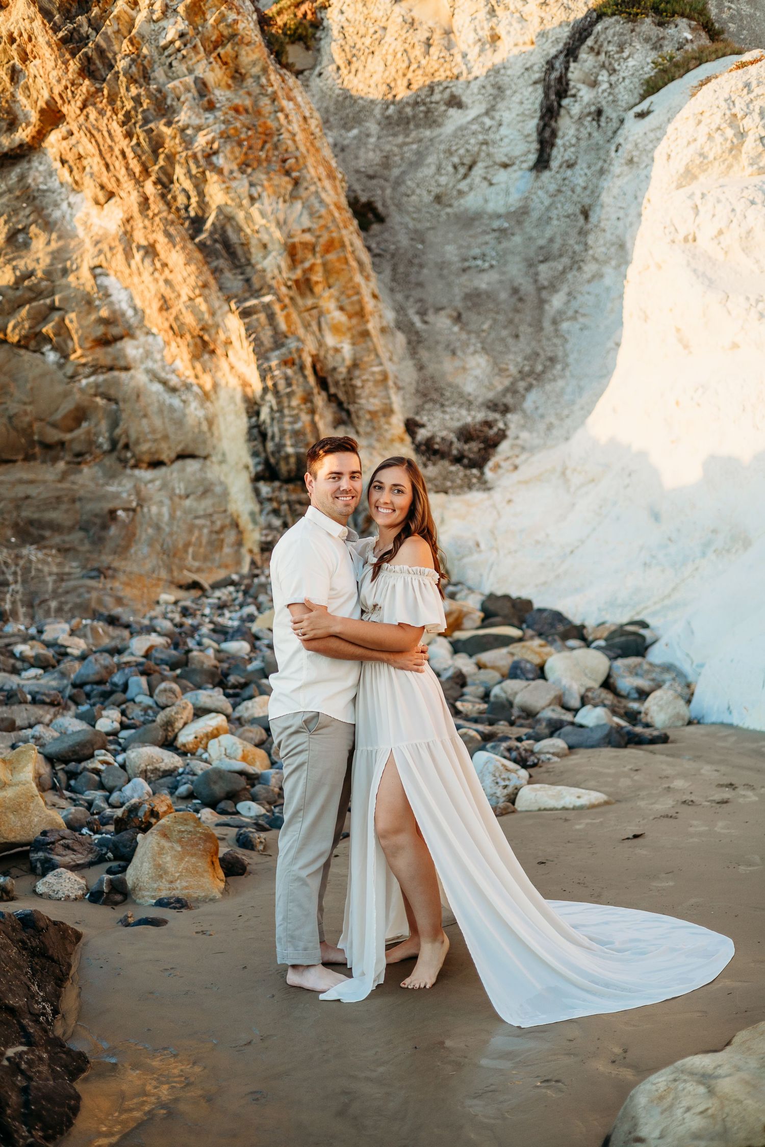 A couple poses together against dramatic coastal cliffs at sunset.