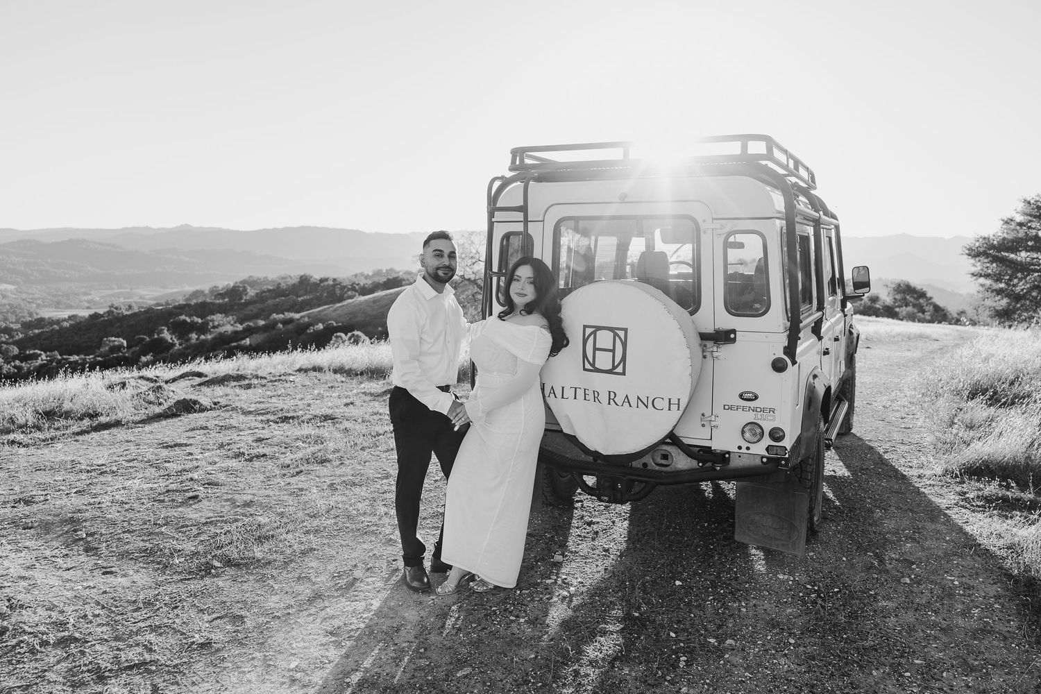 Black and white photos showing a couple embracing outdoors with a vintage camper trailer in the background.
