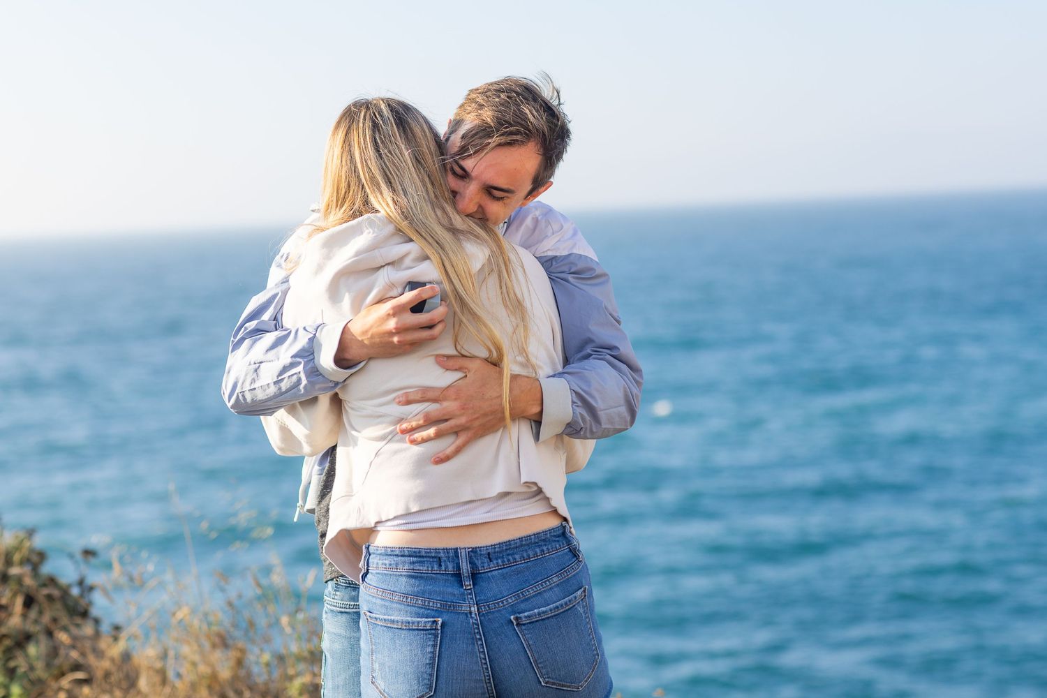 A couple sharing an emotional hug on a cliff overlooking the ocean.