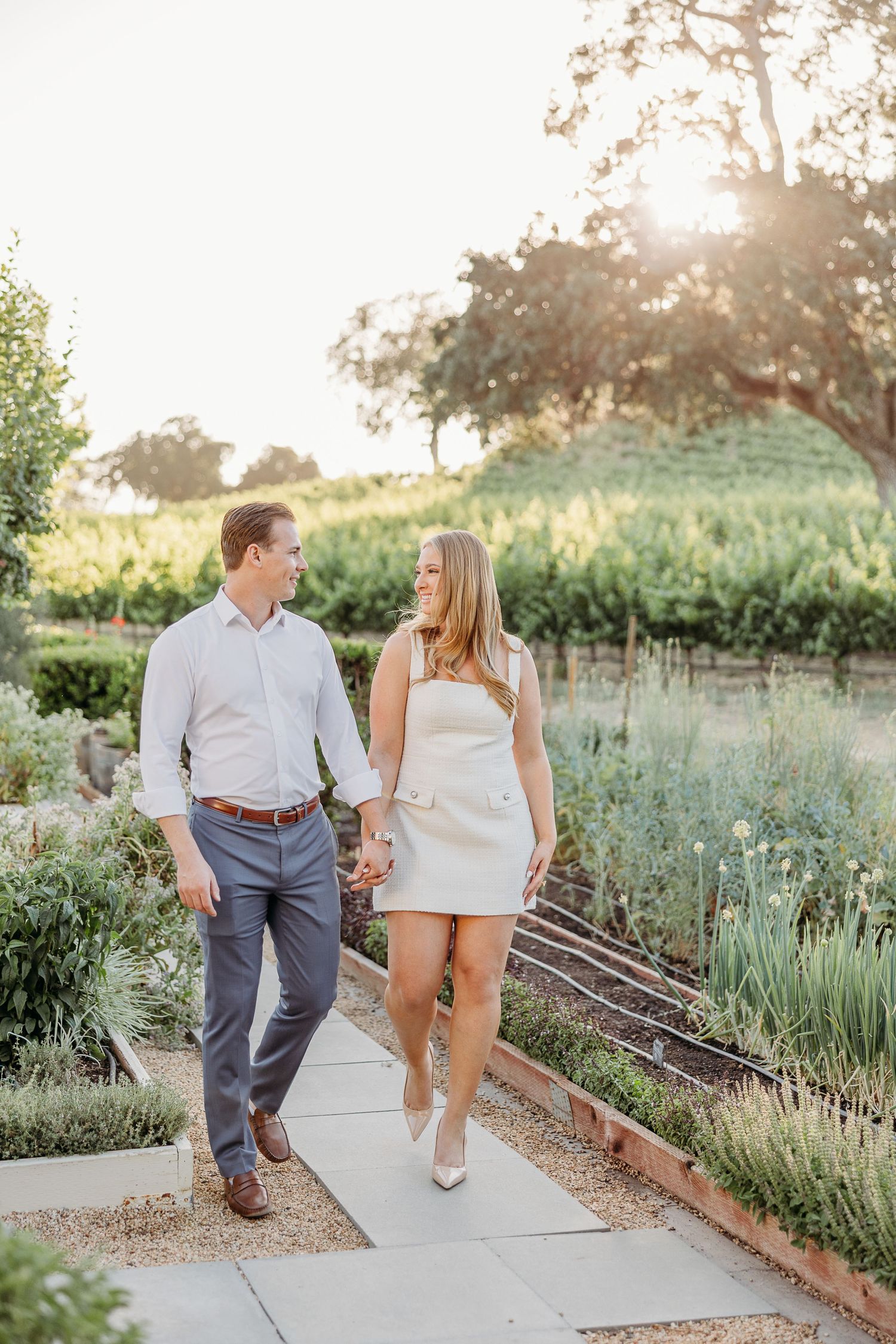 Couple walking together on garden pathway during golden hour in romantic outdoor setting.