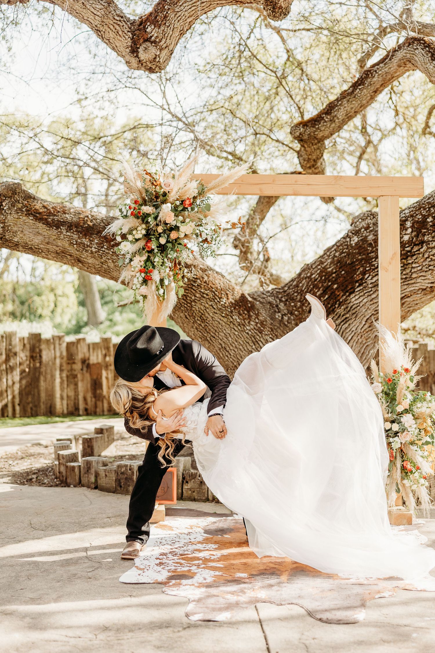 A dip-kiss pose under a decorated tree arch during an outdoor wedding ceremony.