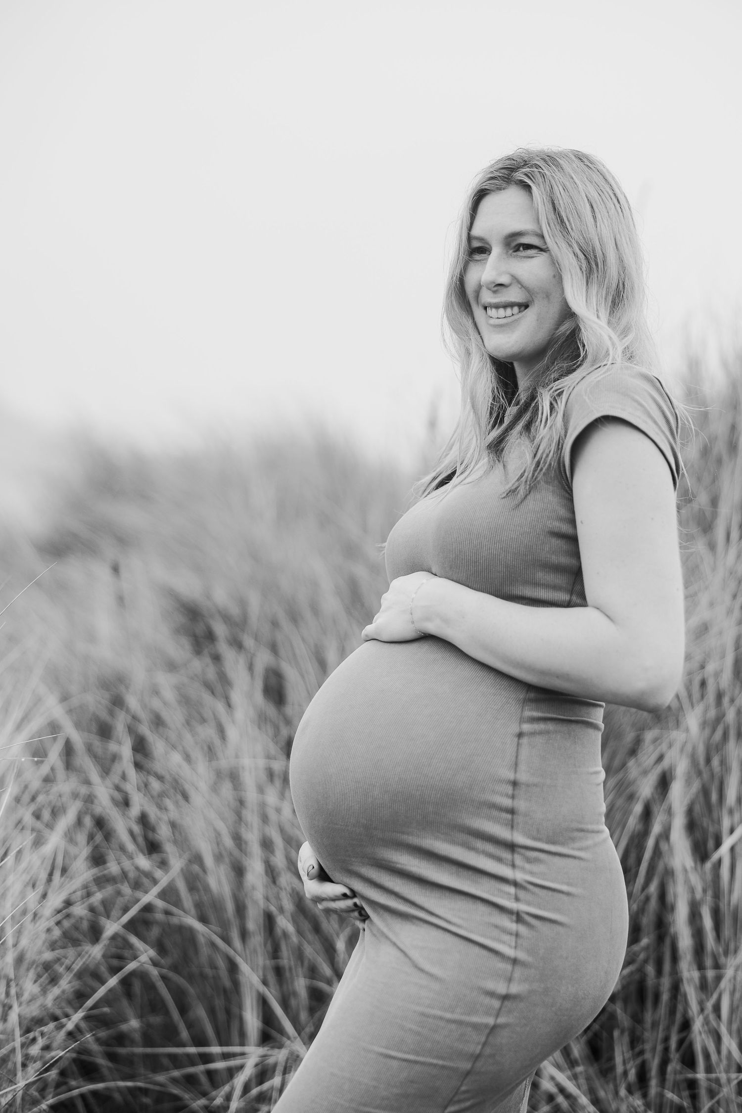 Side view maternity portrait in black and white showing a pregnant woman's profile against a light background.