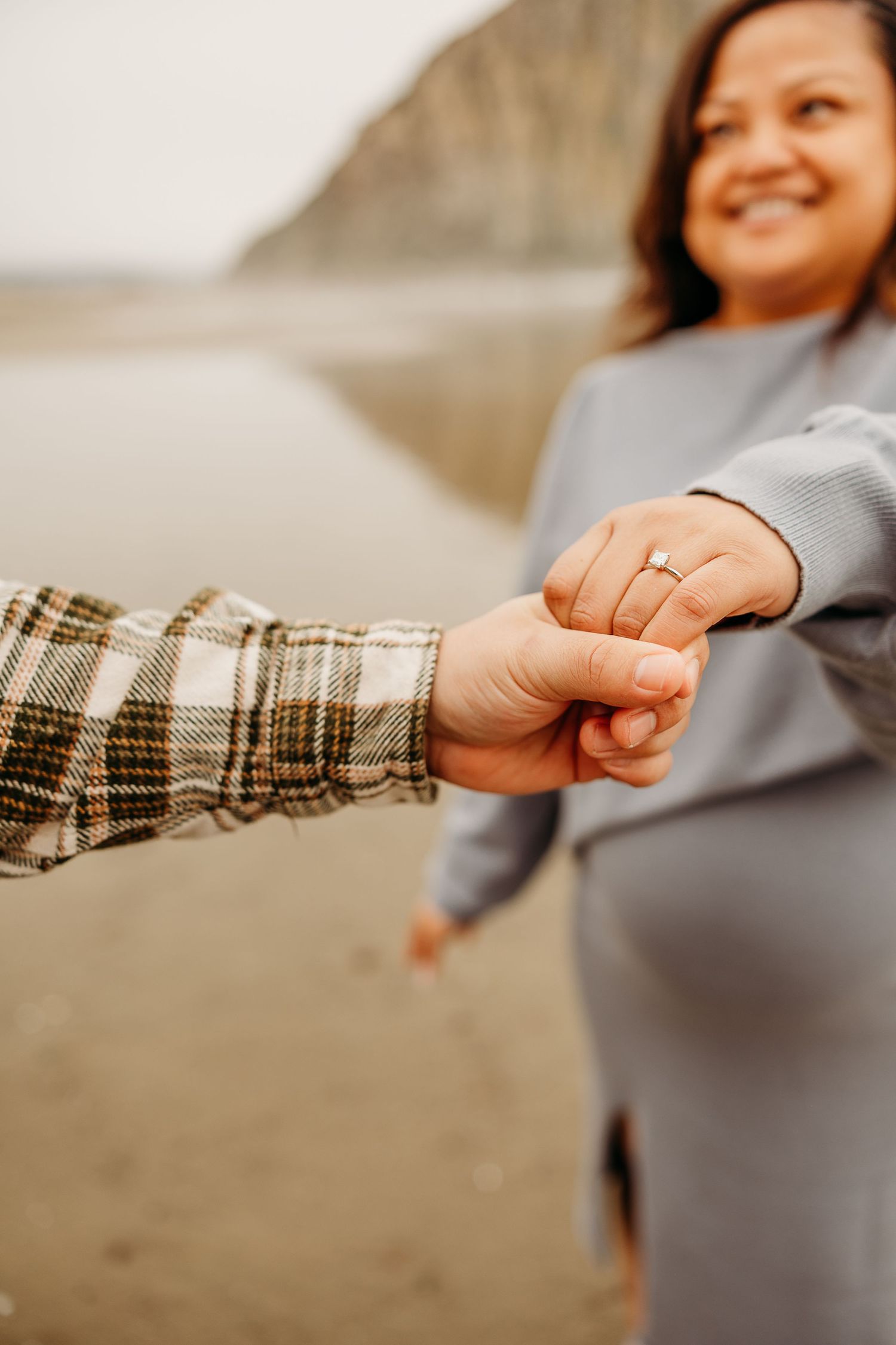 Close-up of hands holding together on a beach with cliffs visible in the background.