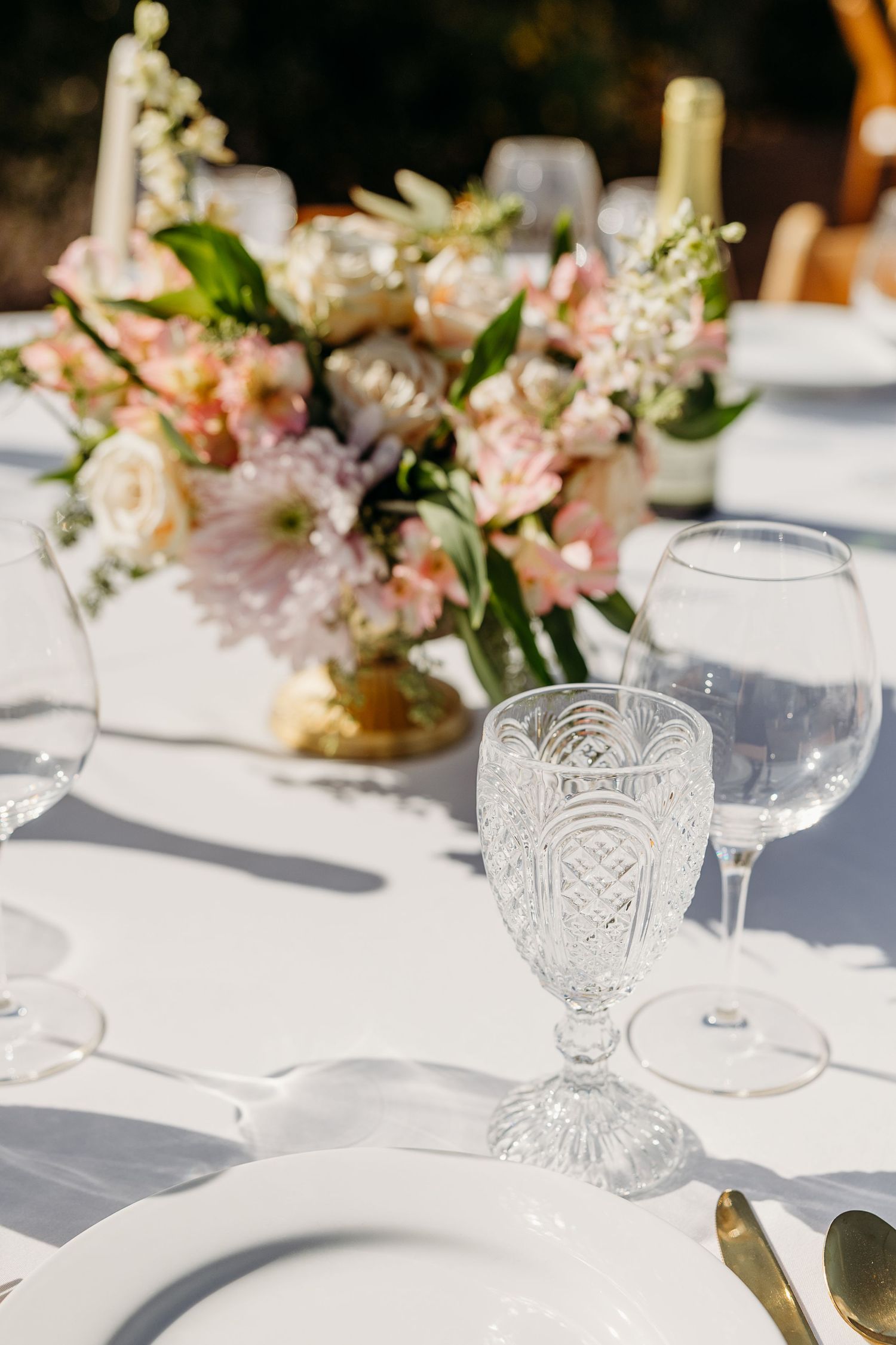 Elegant table setting with crystal glasses and pink floral centerpieces on white tablecloth.
