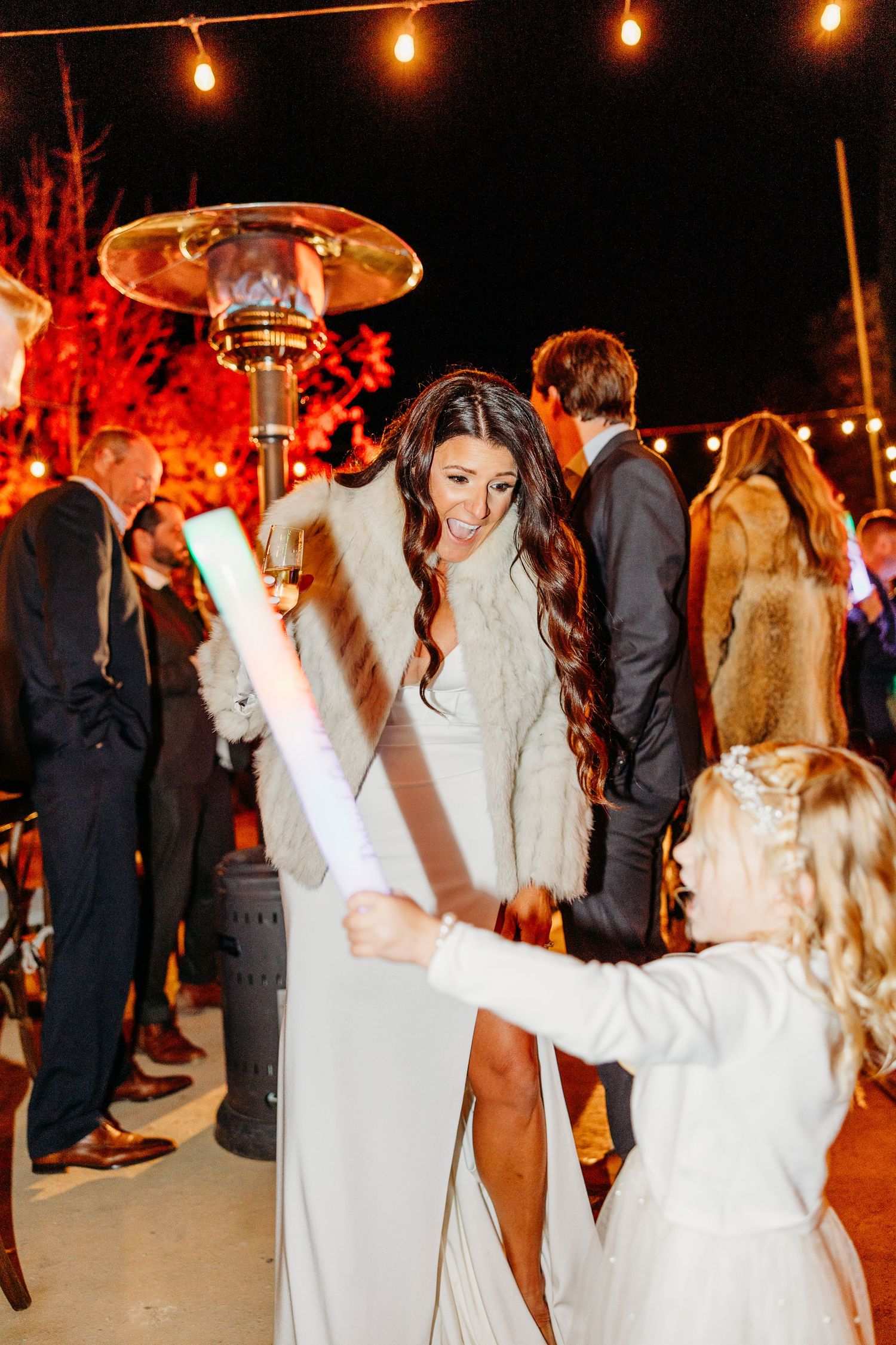 Wedding guests dance and celebrate on an outdoor dance floor illuminated by warm string lights overhead.