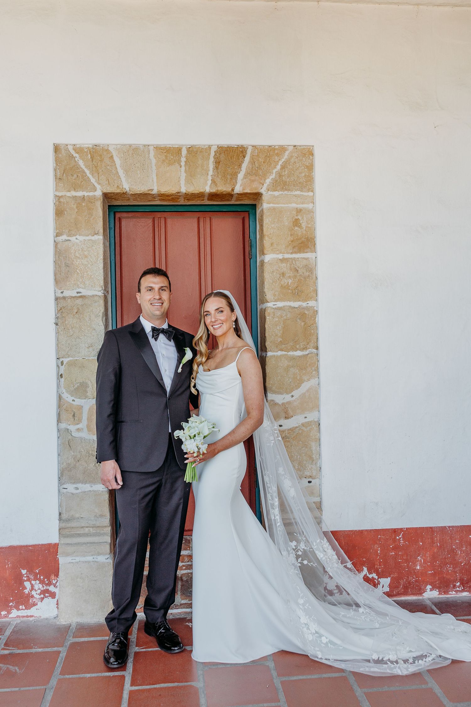 A formal wedding portrait in front of a rustic doorway with stone archway and red trim.
