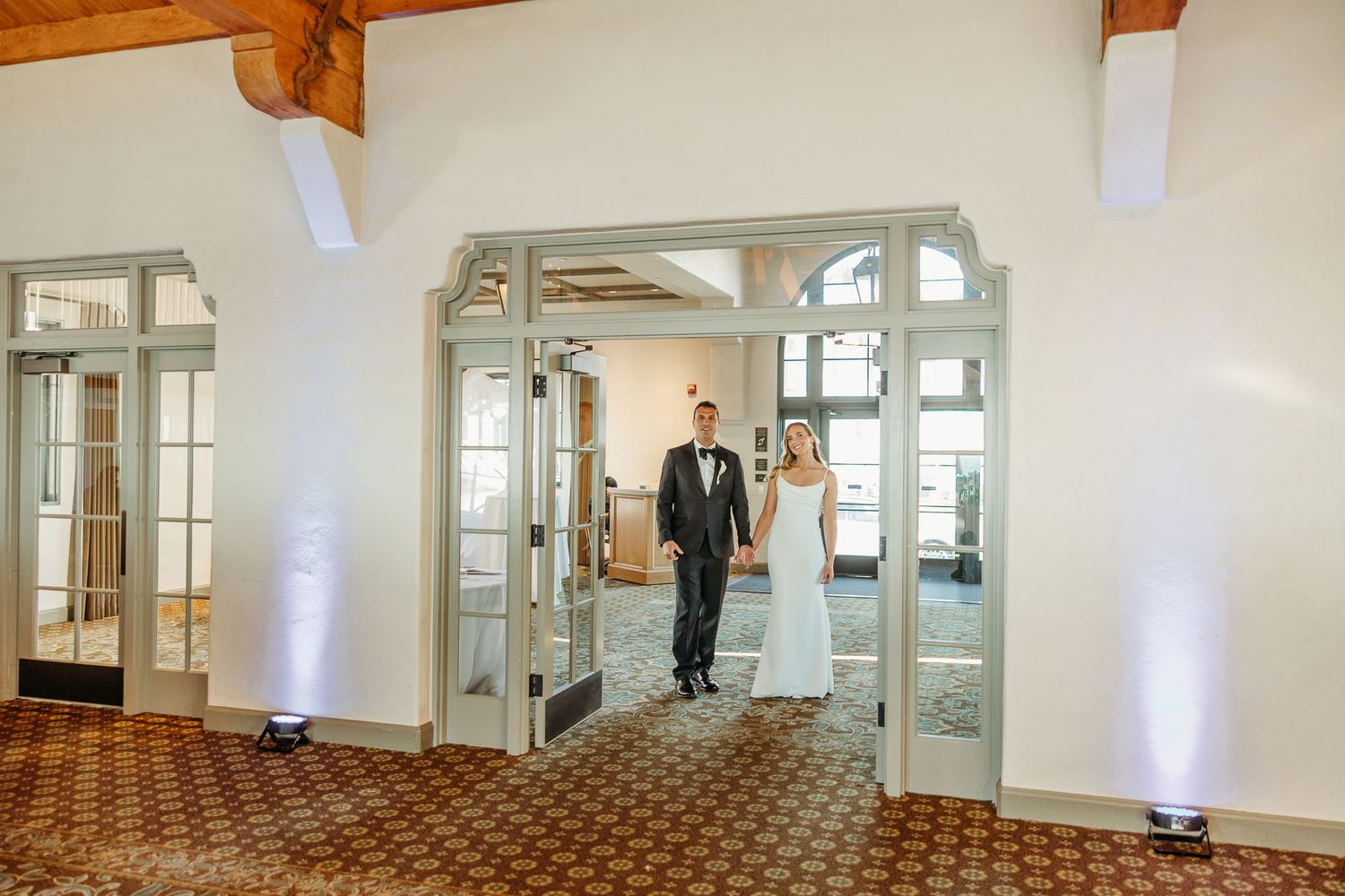 A couple stands in an elegant doorway with French doors and uplighting.