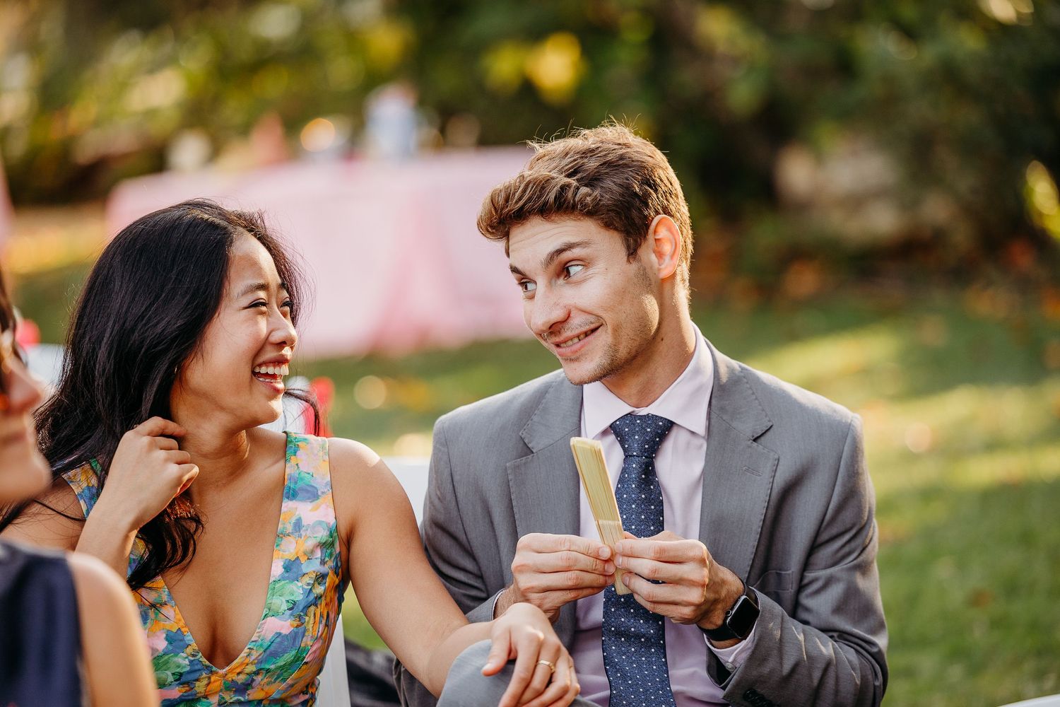 Two wedding guests share a lighthearted moment while enjoying drinks outdoors.