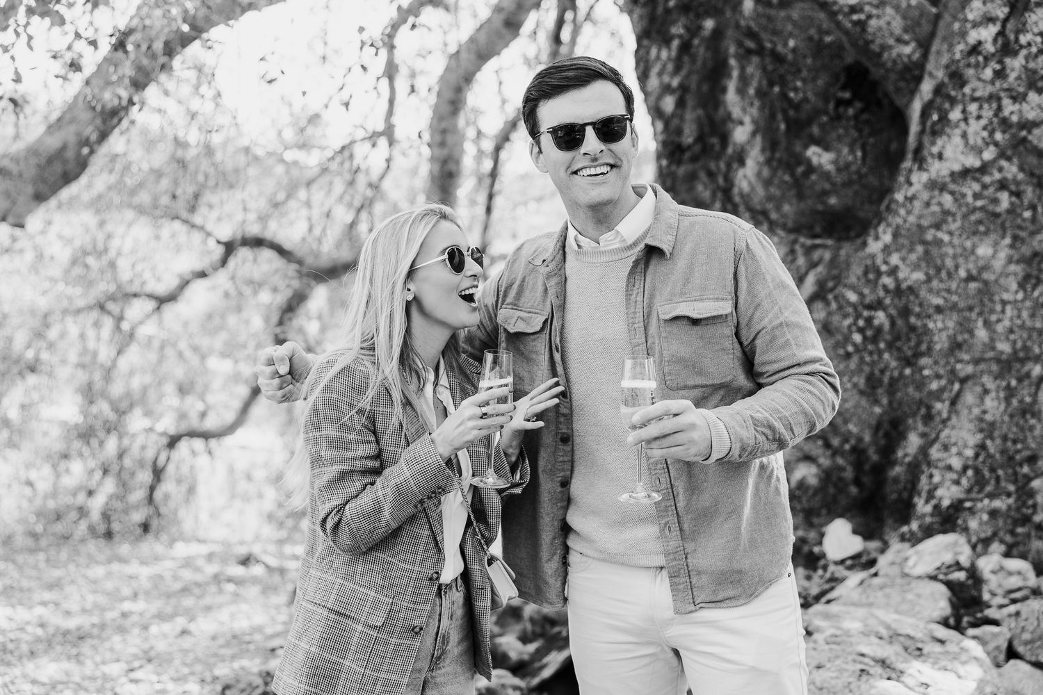 Black and white photo of a couple sharing a tender moment outdoors among oak trees.