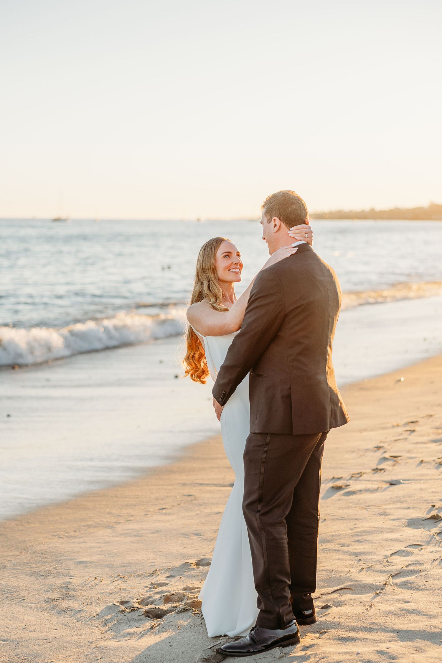 A couple embraces on the beach at sunset during their wedding photoshoot.