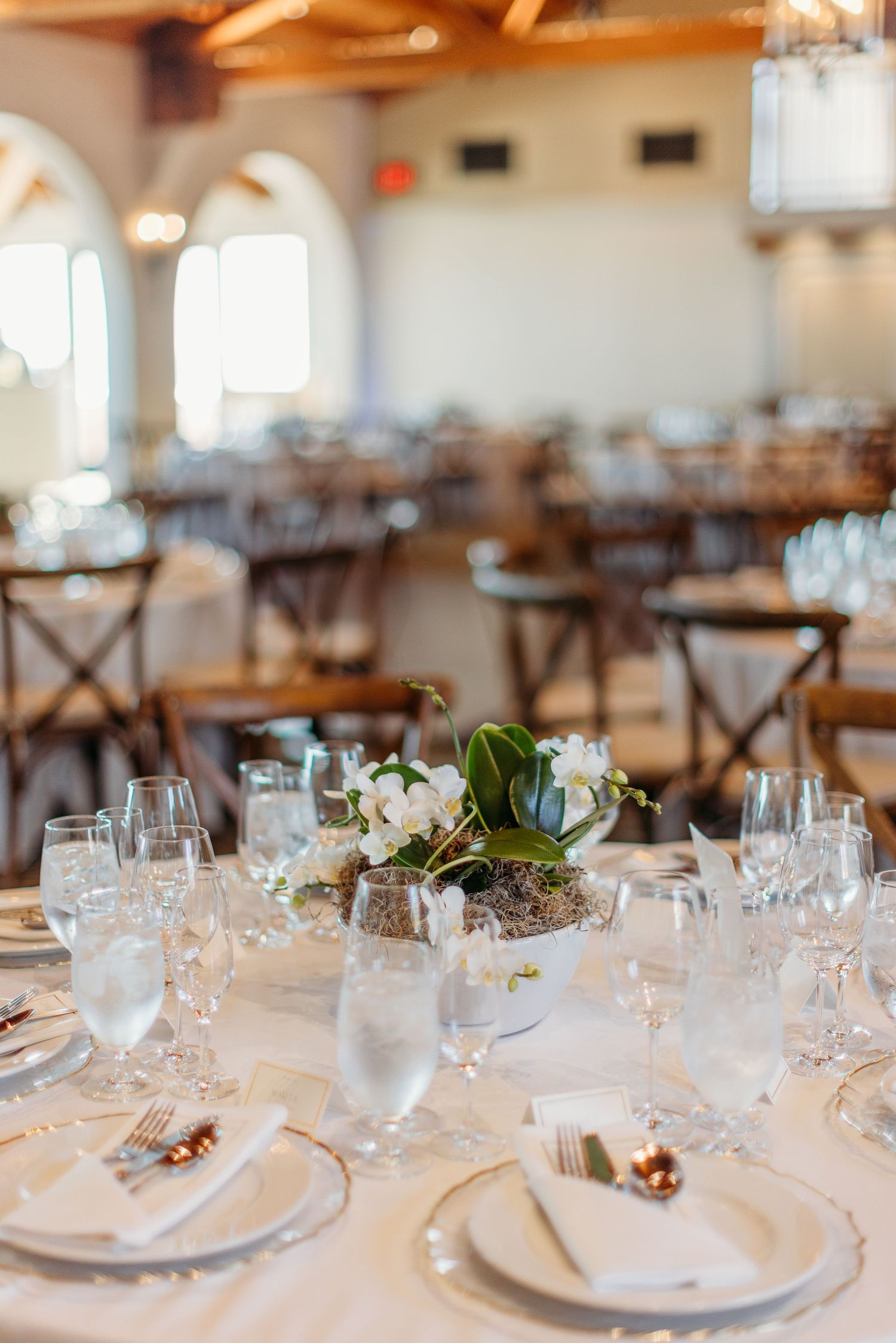 An elegant wedding reception table setting with white linens, glassware and floral centerpieces.