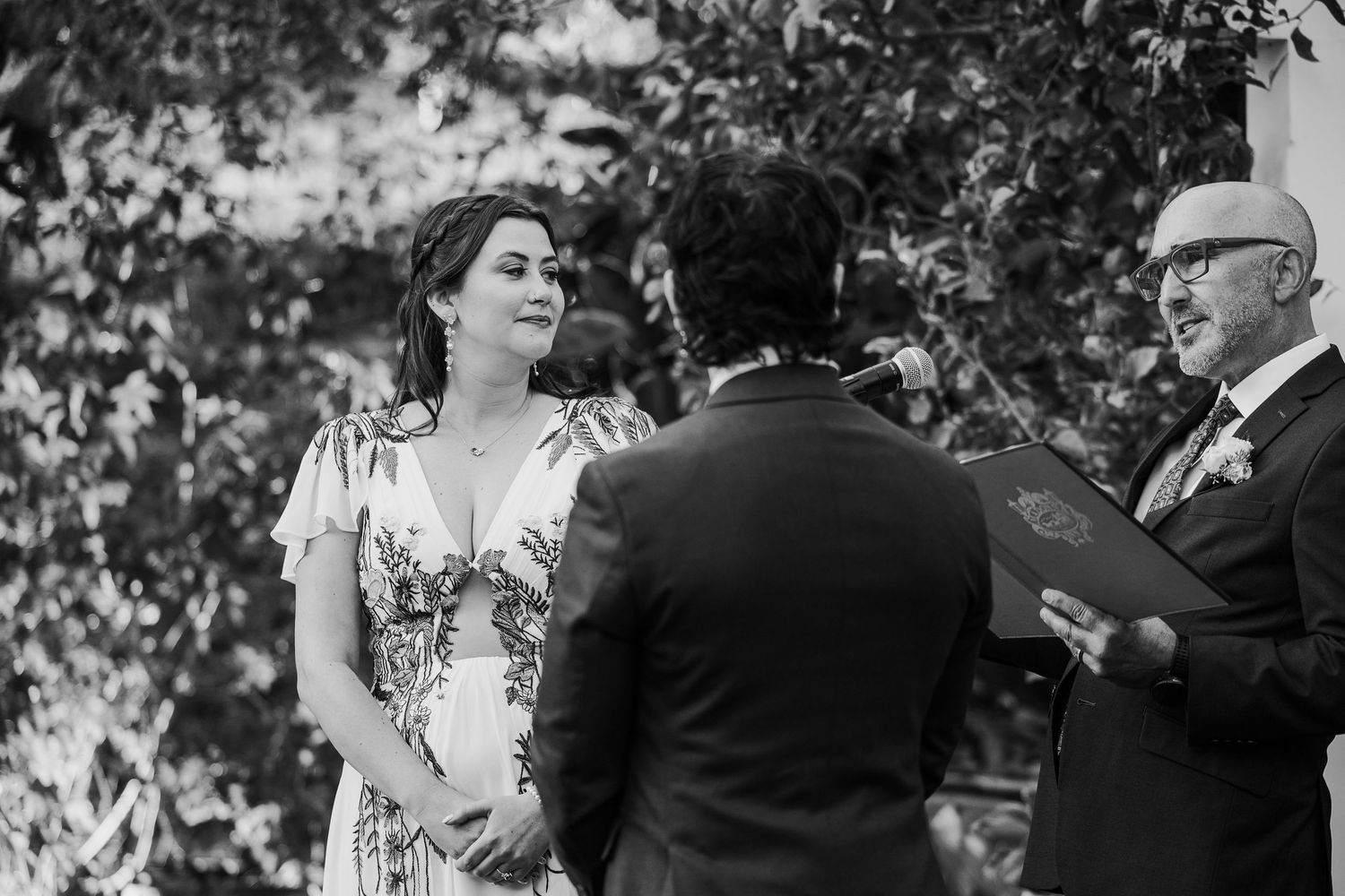 A black and white photo captures an intimate outdoor wedding ceremony moment.