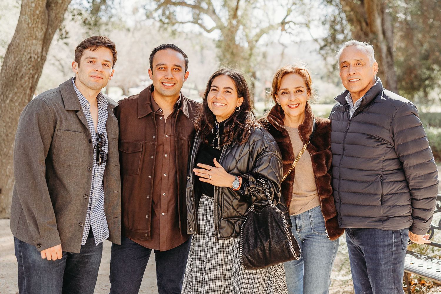 A group of five people standing together outdoors on a sunny winter day wearing casual jackets and sweaters.