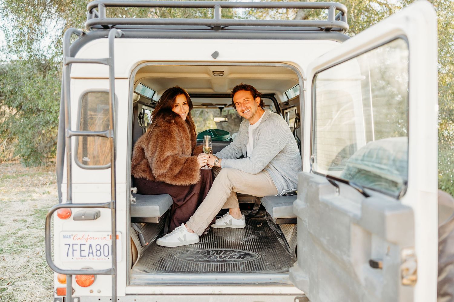 A couple poses together inside a vintage Land Rover Defender with panoramic mountain views.