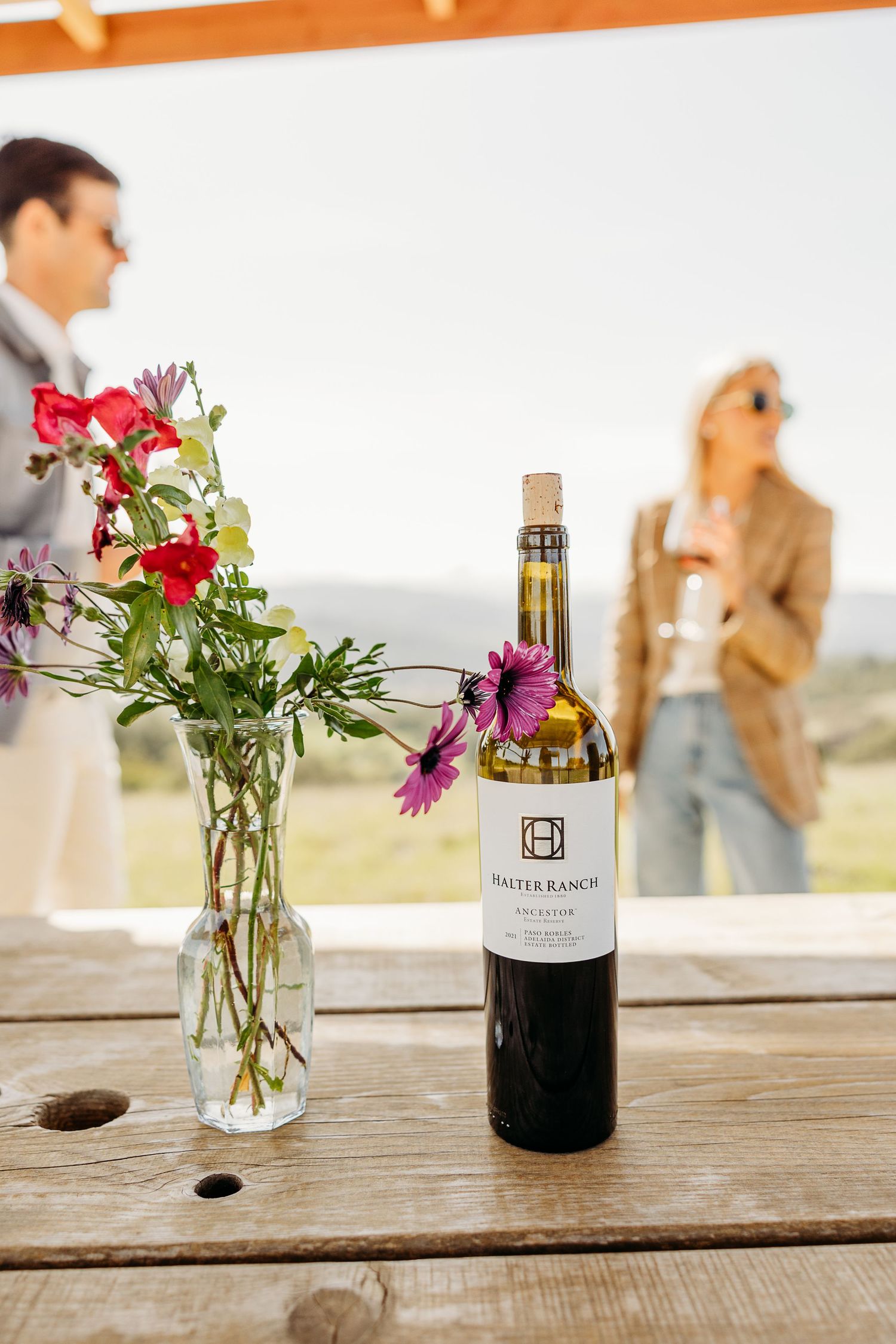 Wine bottles and colorful flower arrangements displayed on rustic wooden table.