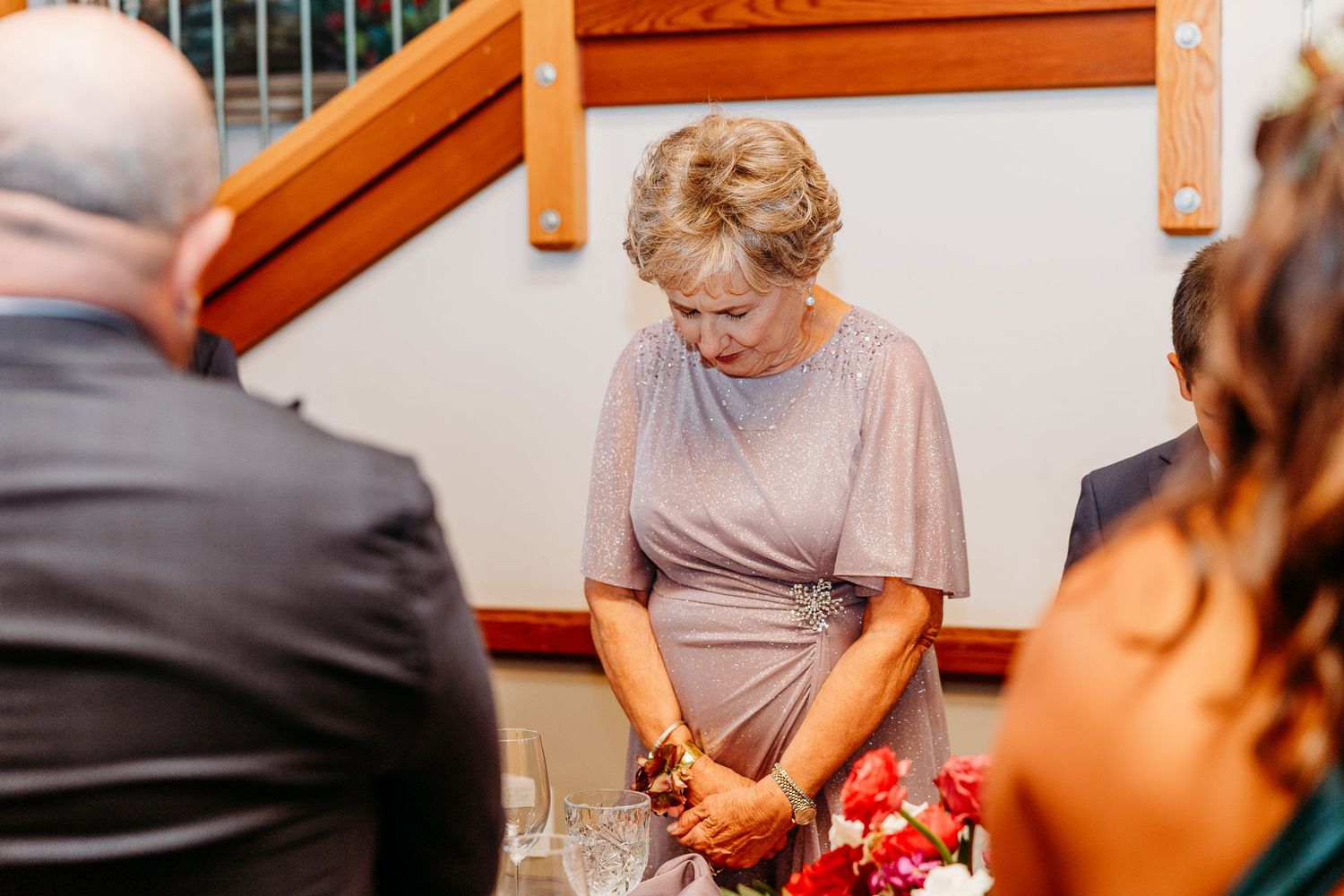 Wedding reception guests gathered around tables with red decor and centerpieces.
