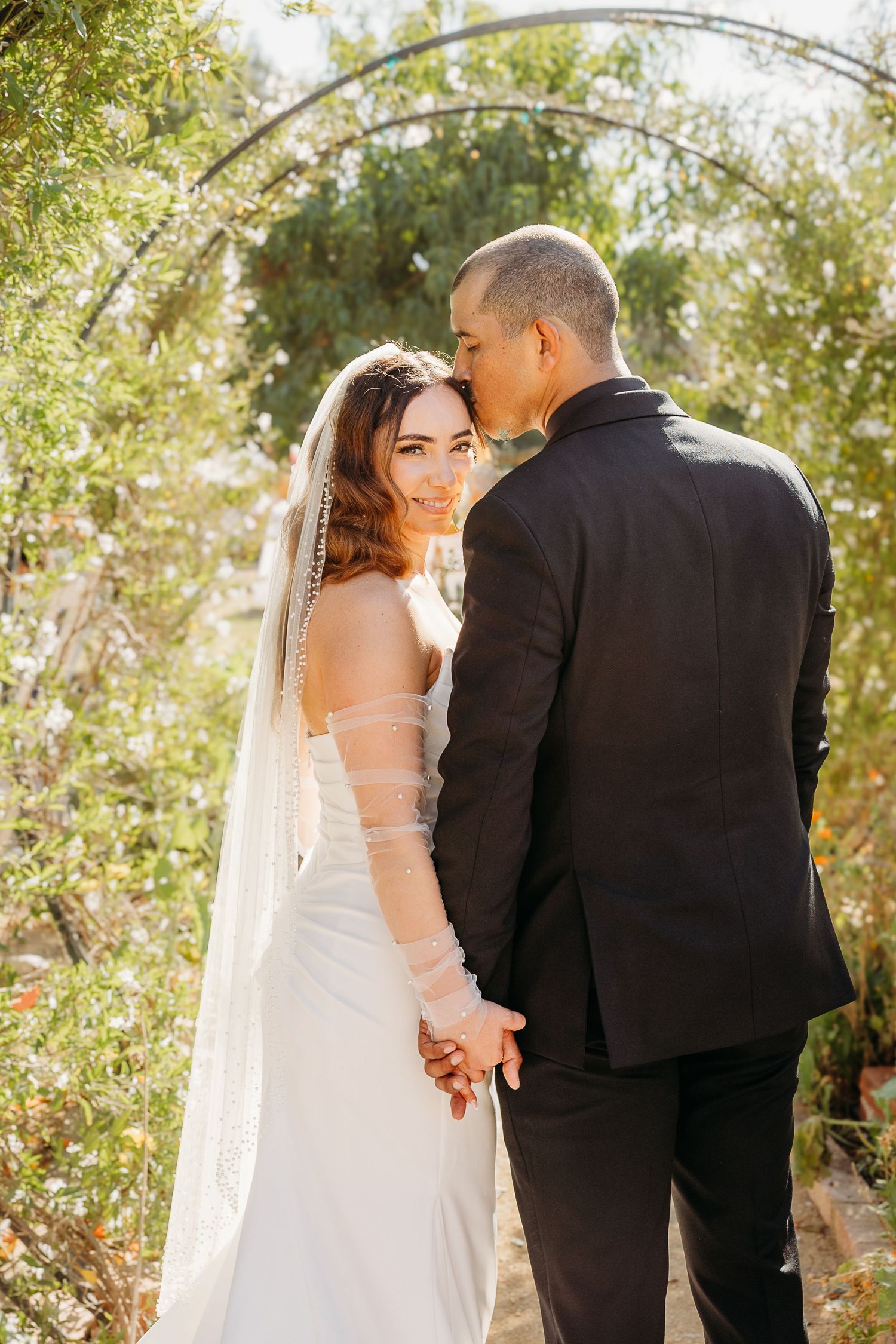 Wedding couple walking together outdoors under natural sunlight and trees.