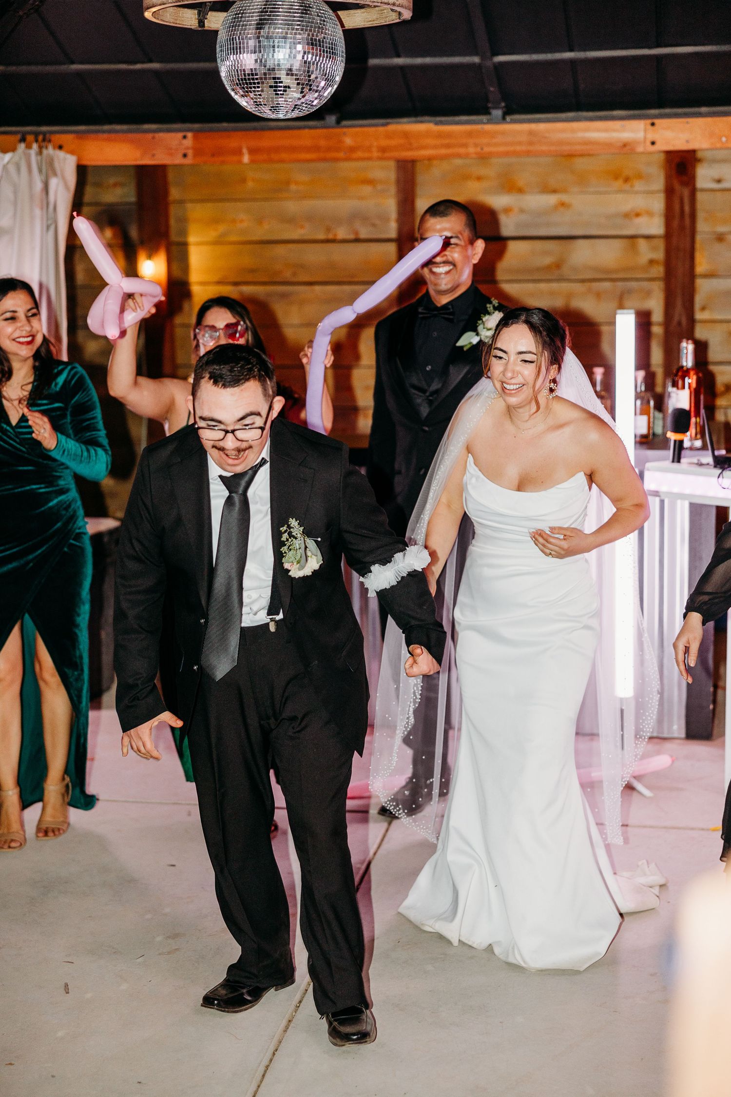 Wedding guests dancing under a disco ball in a rustic wooden venue.
