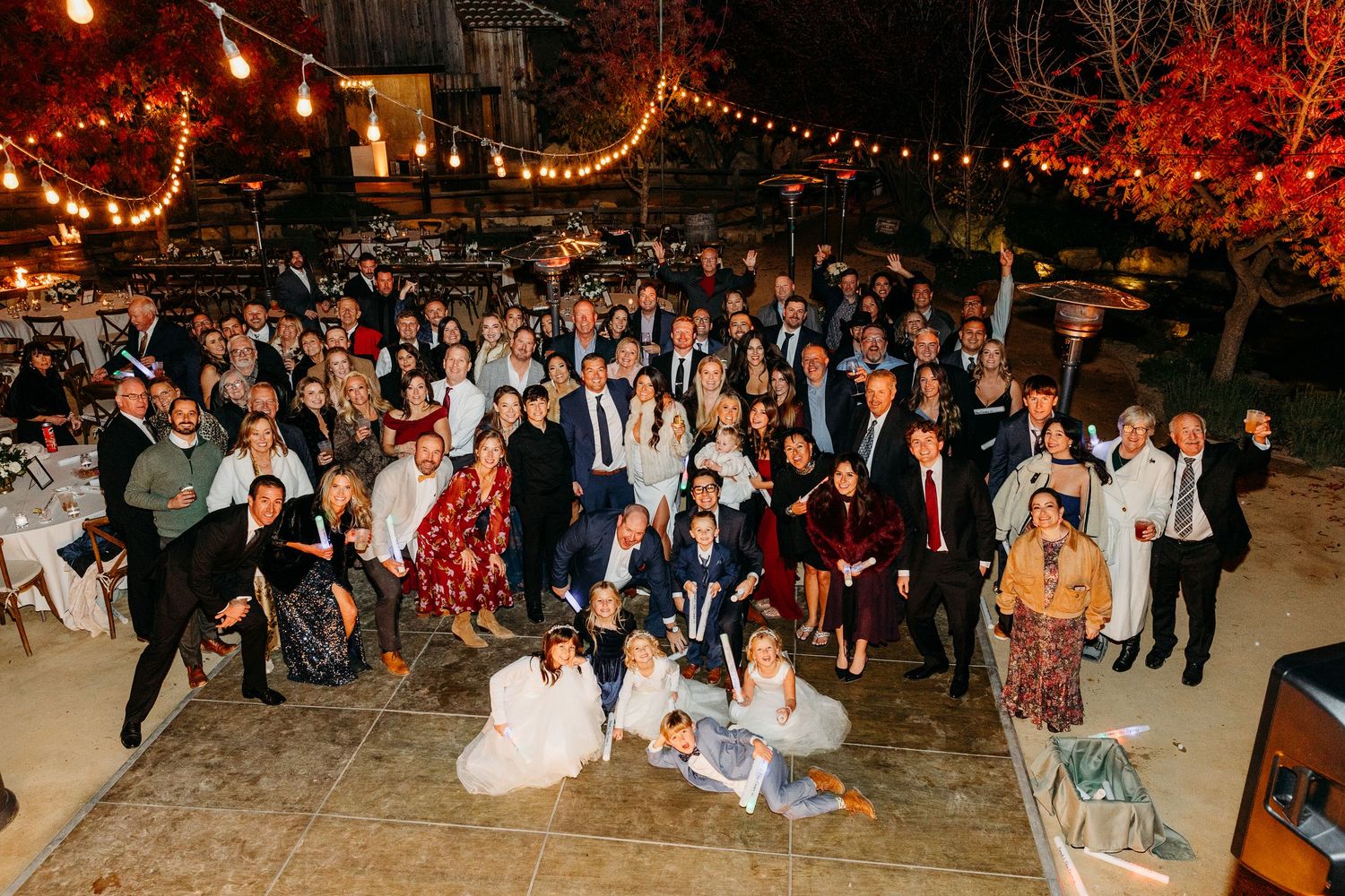 Wedding reception crowd celebrates under string lights at an outdoor evening party.