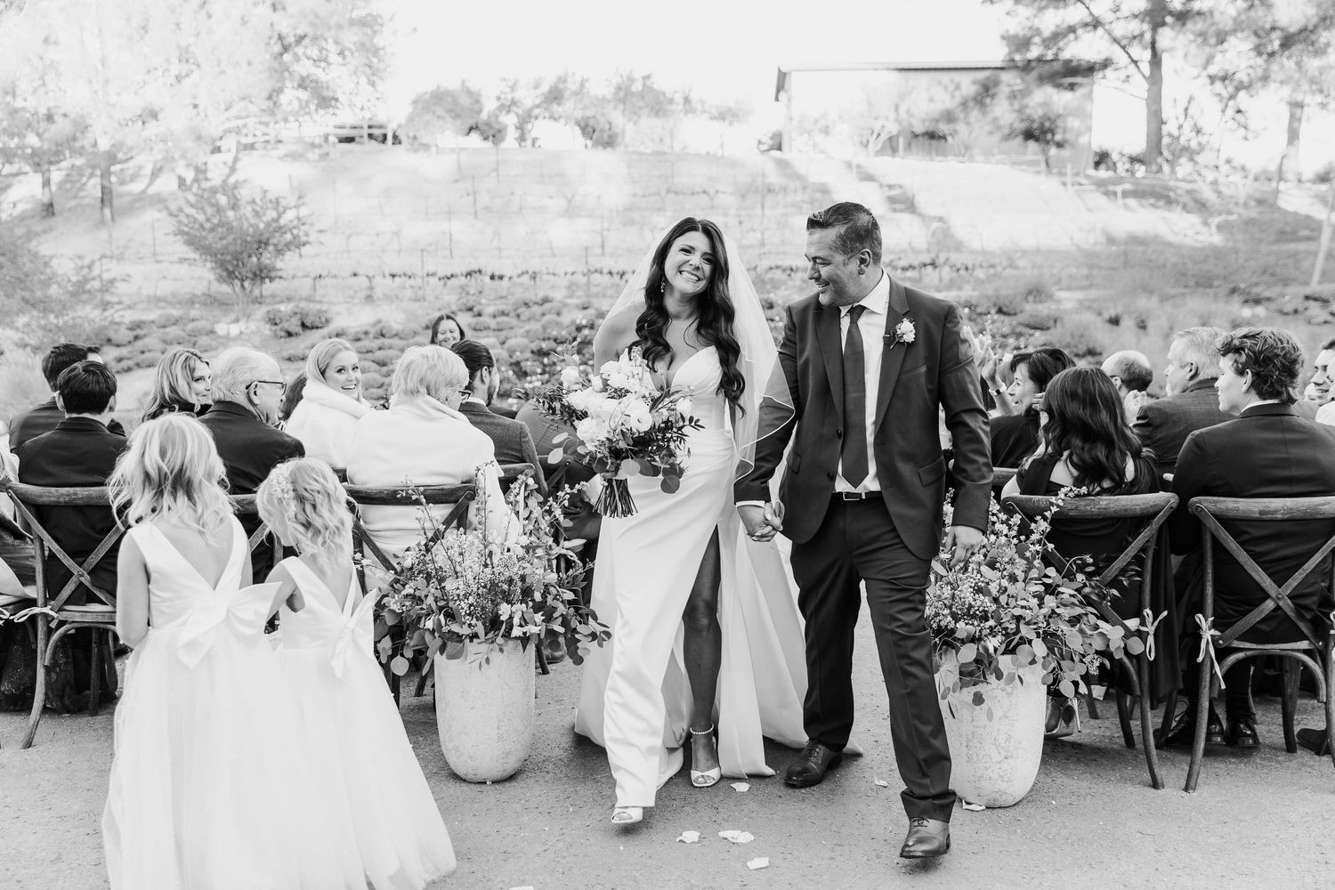 Outdoor wedding ceremony setup with guests seated in wooden chairs against a desert landscape.