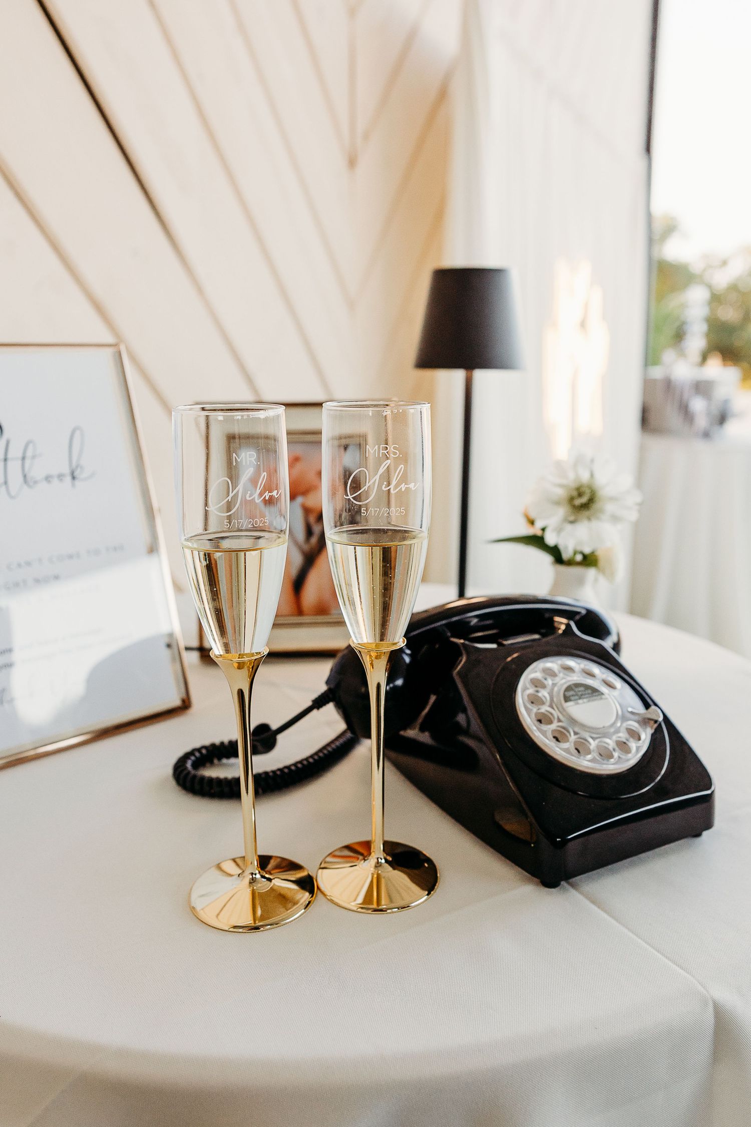 Vintage black rotary telephone with champagne glasses and elegant gold decor on white surface.
