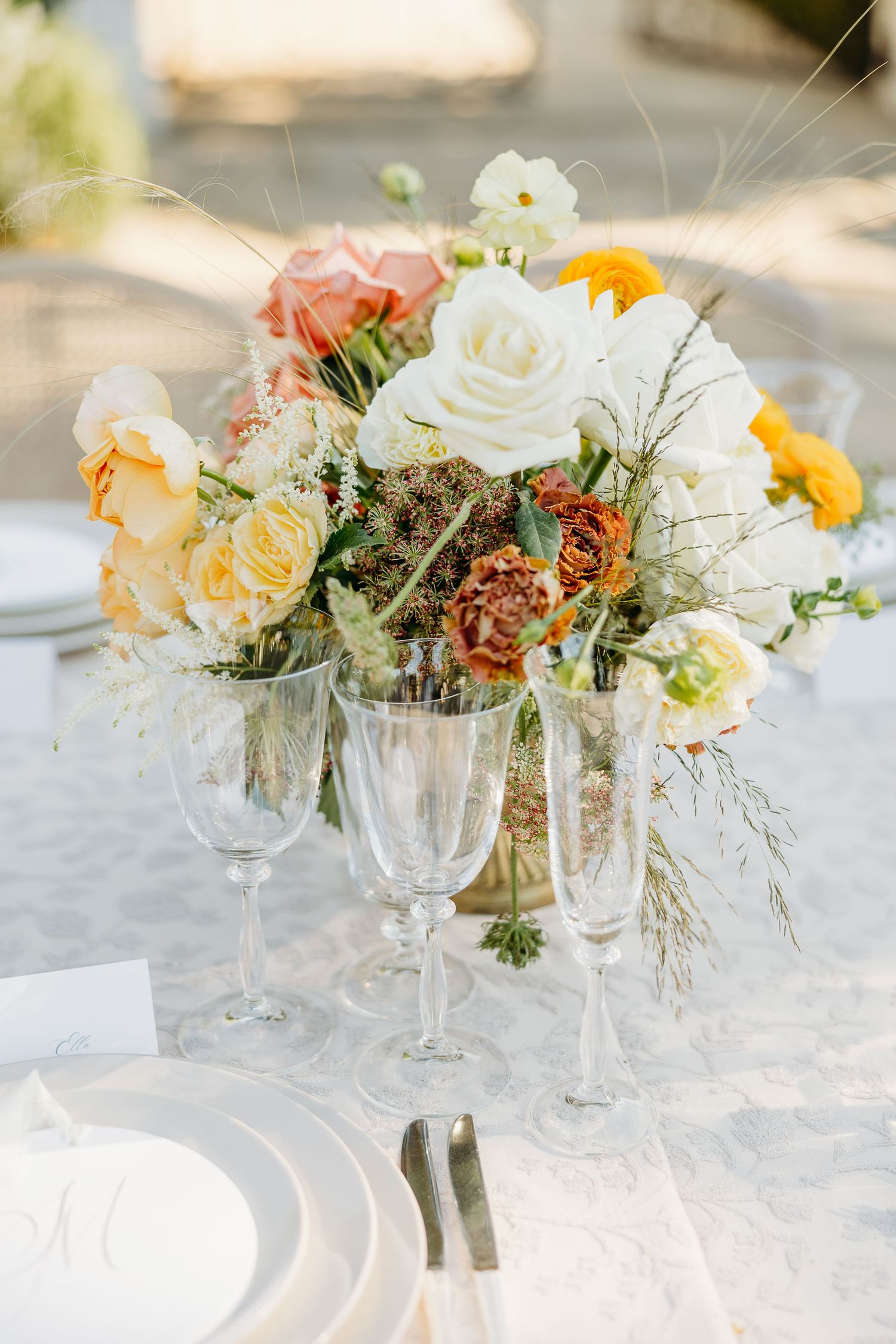 Elegant table settings with crystal glasses and delicate floral centerpieces in white and peach tones on a white tablecloth.