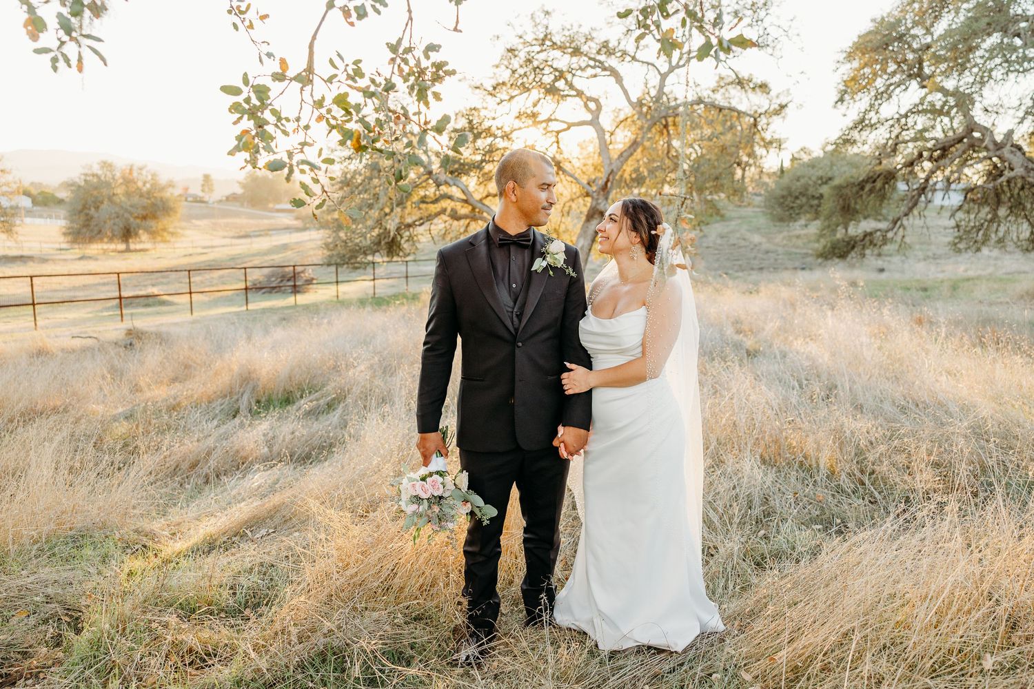 Newlyweds walking through golden grass field during sunset portrait session.