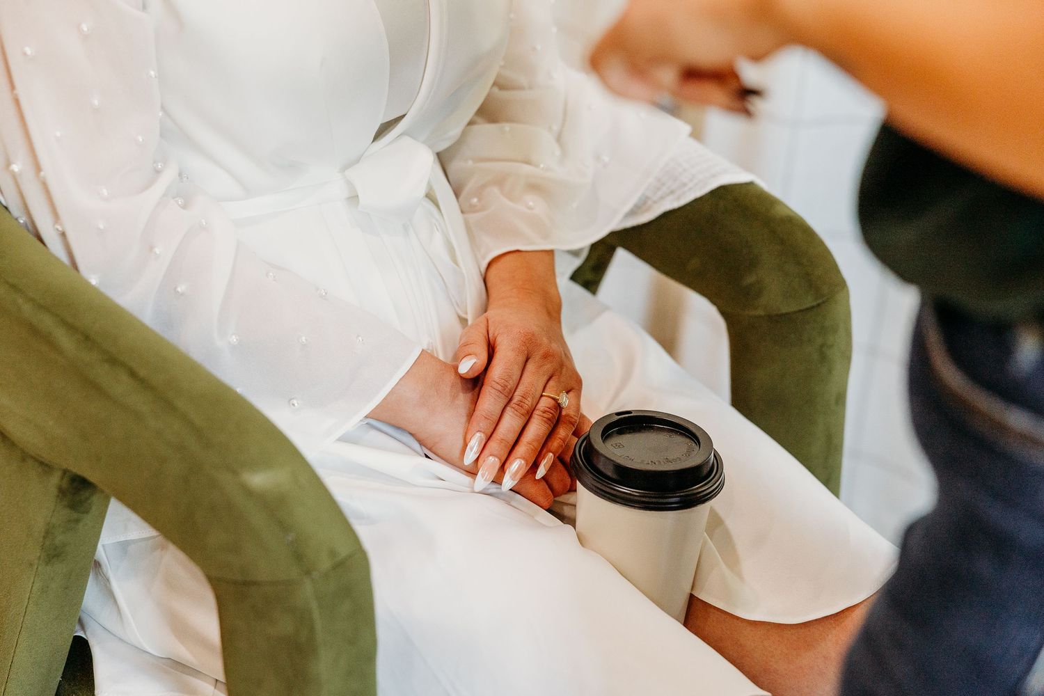 Close-up view of hands holding white ceramic coffee cups against a light background.